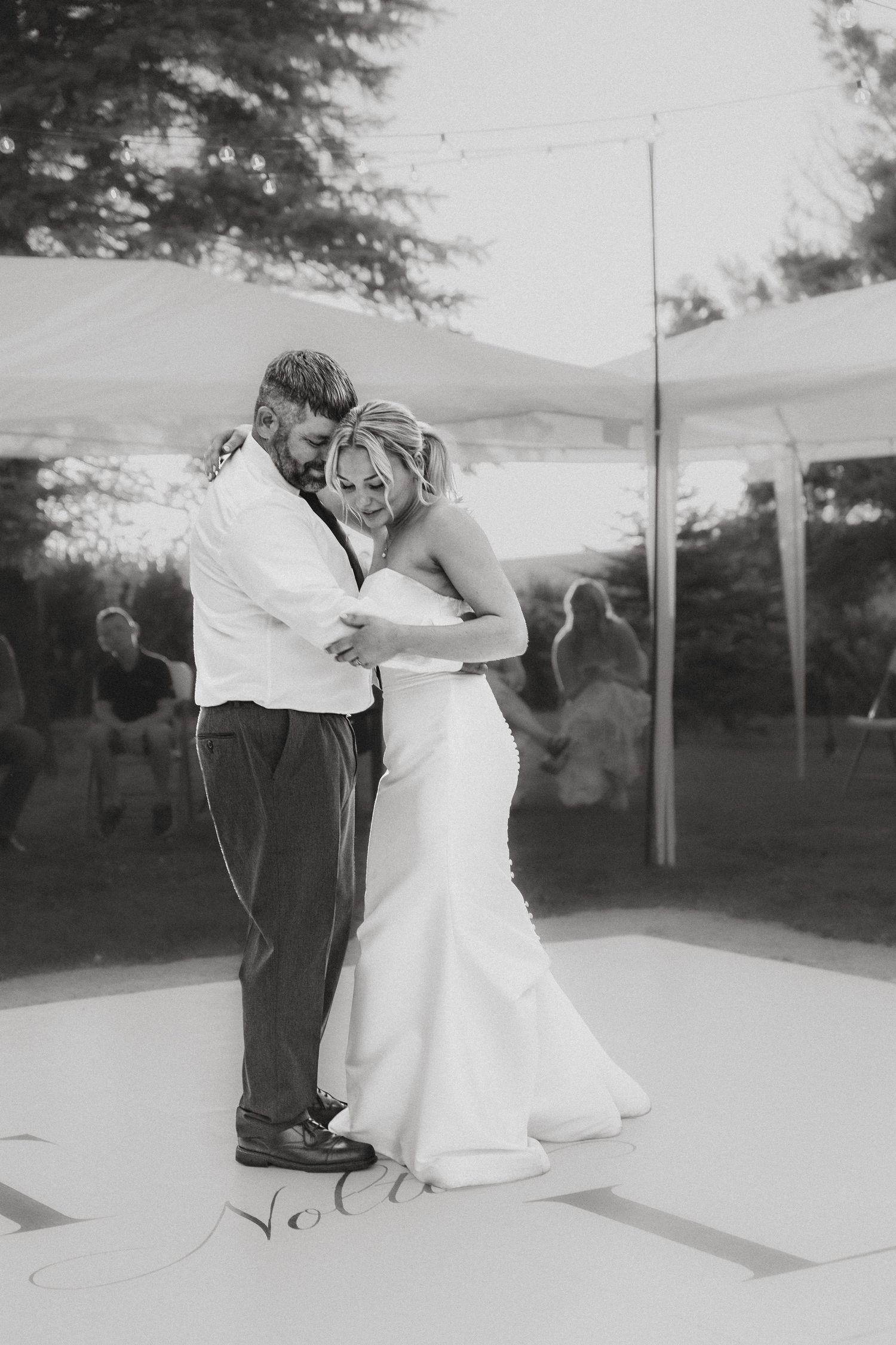 Black and white photo of bride and groom sharing intimate first dance under a tent at outdoor reception.