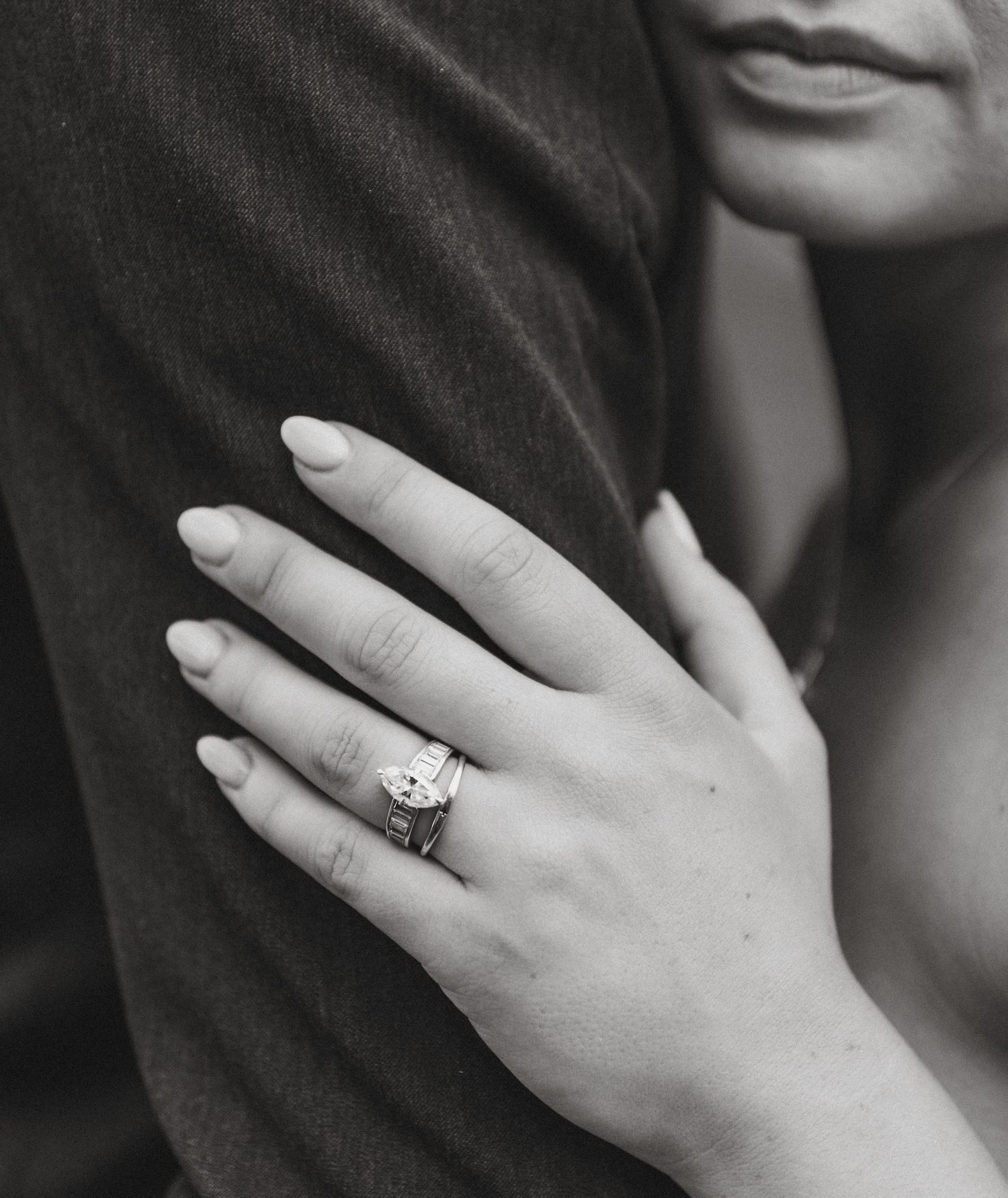 Black and white photo of a woman showcasing an elegant diamond engagement ring while embracing a man.