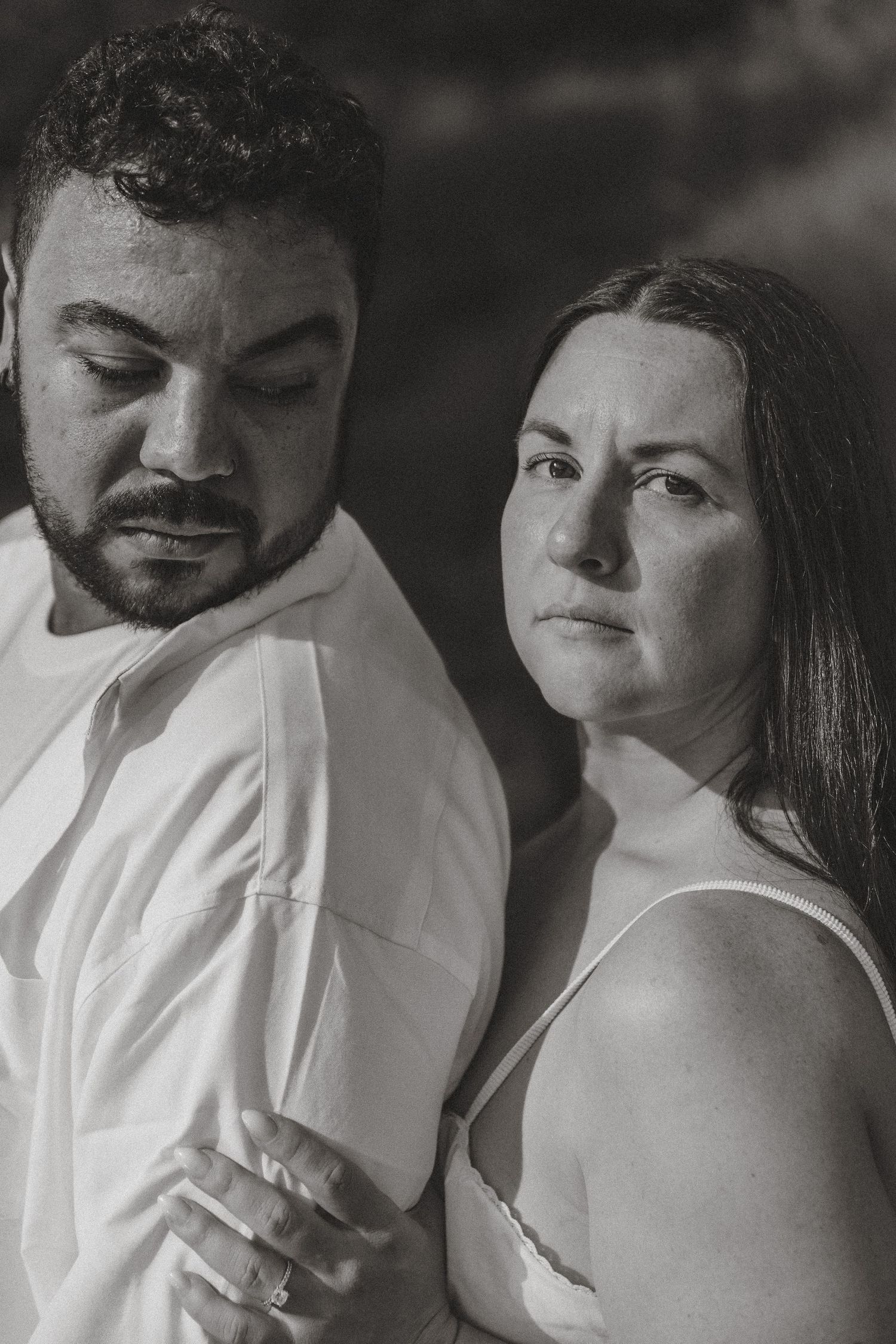 Black and white portrait of a couple in white, woman gazing at camera while man looks down.