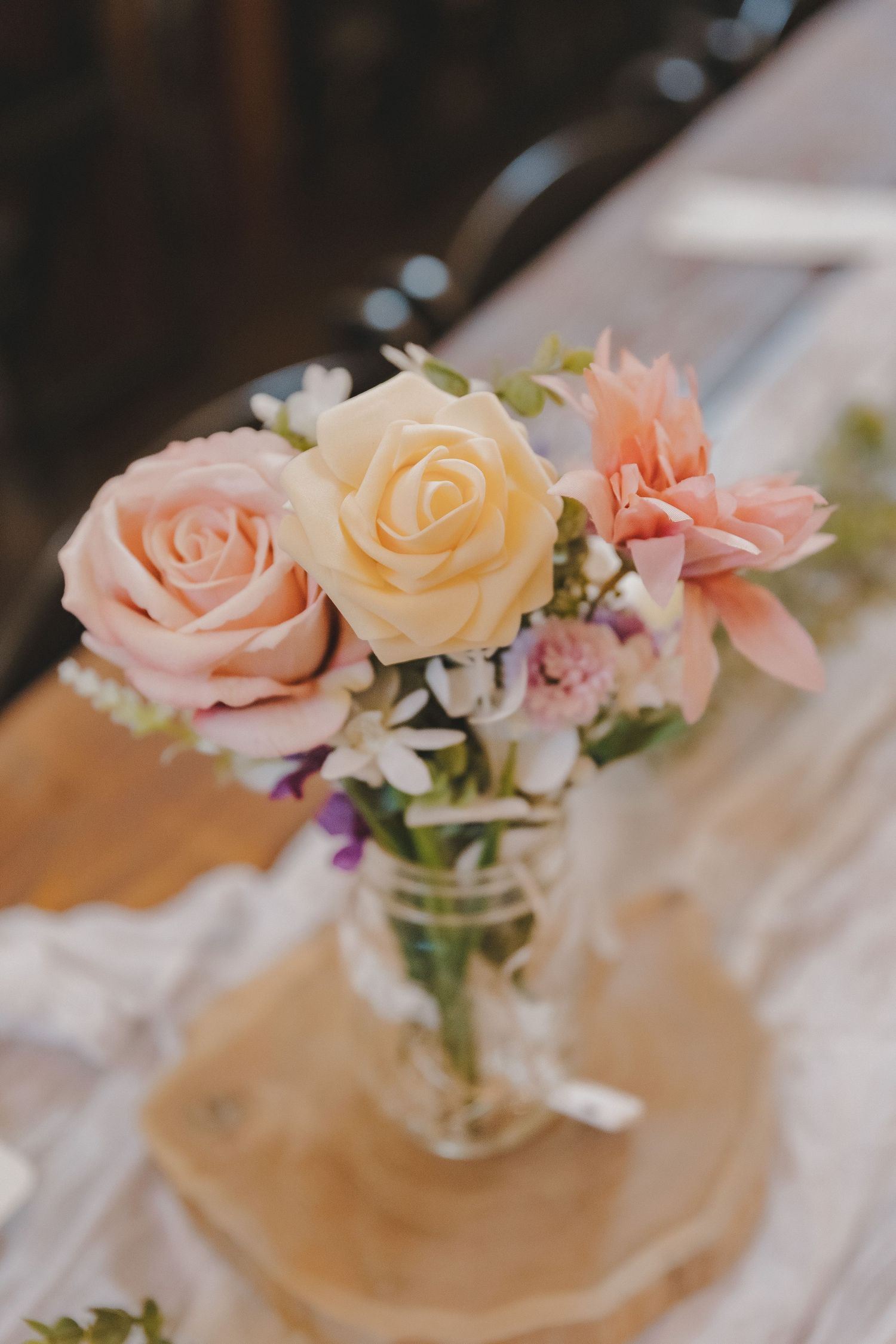 Pastel pink and yellow roses in a mason jar vase centerpiece on a rustic wooden table.