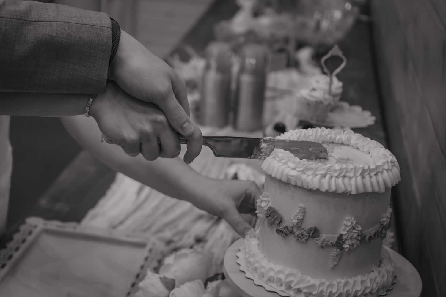 Bride and groom cut elegant white tiered wedding cake in black and white photo.