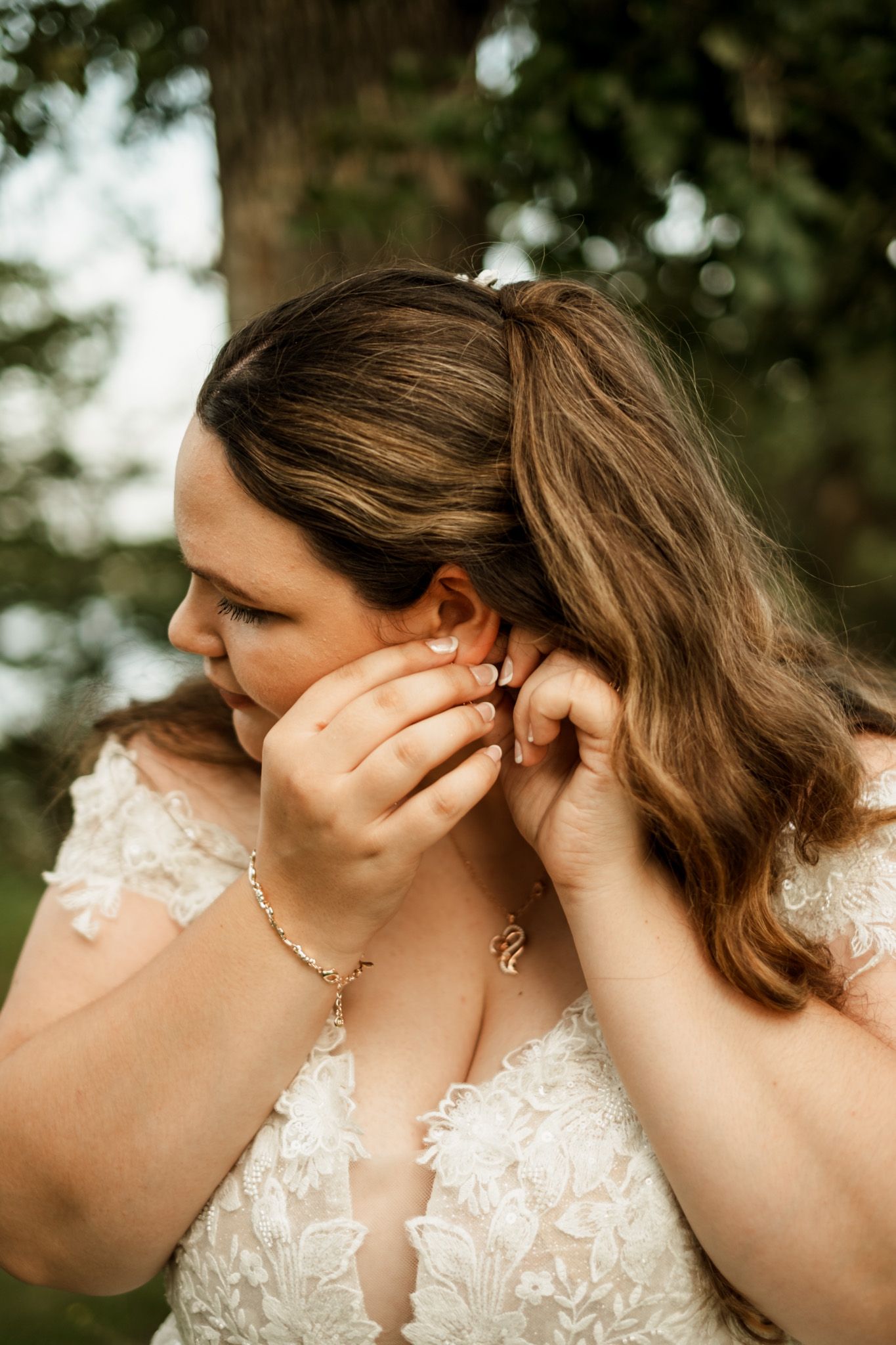 Close-up of a bride putting on earrings while wearing a detailed lace wedding gown.