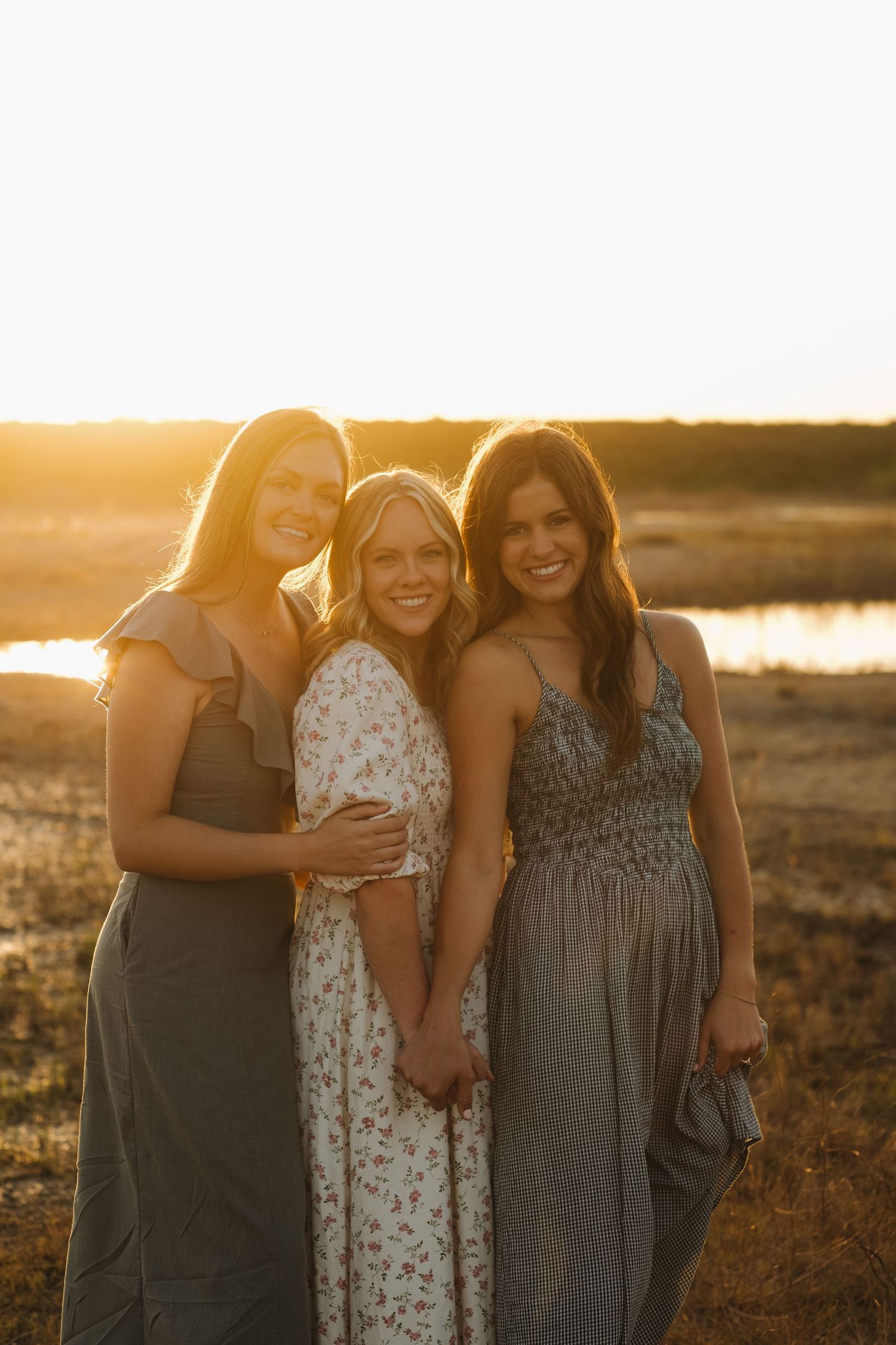 Group of friends in casual dresses gathered together at sunset by a lake.