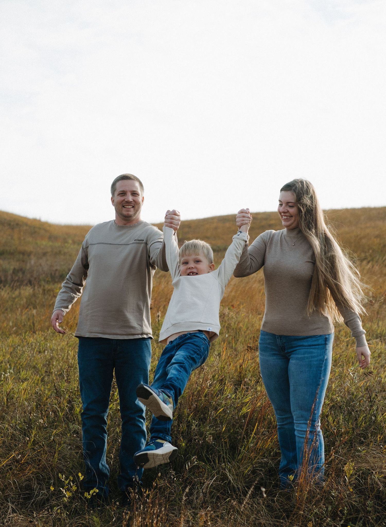 A family holds hands and swings their child while walking through a meadow.