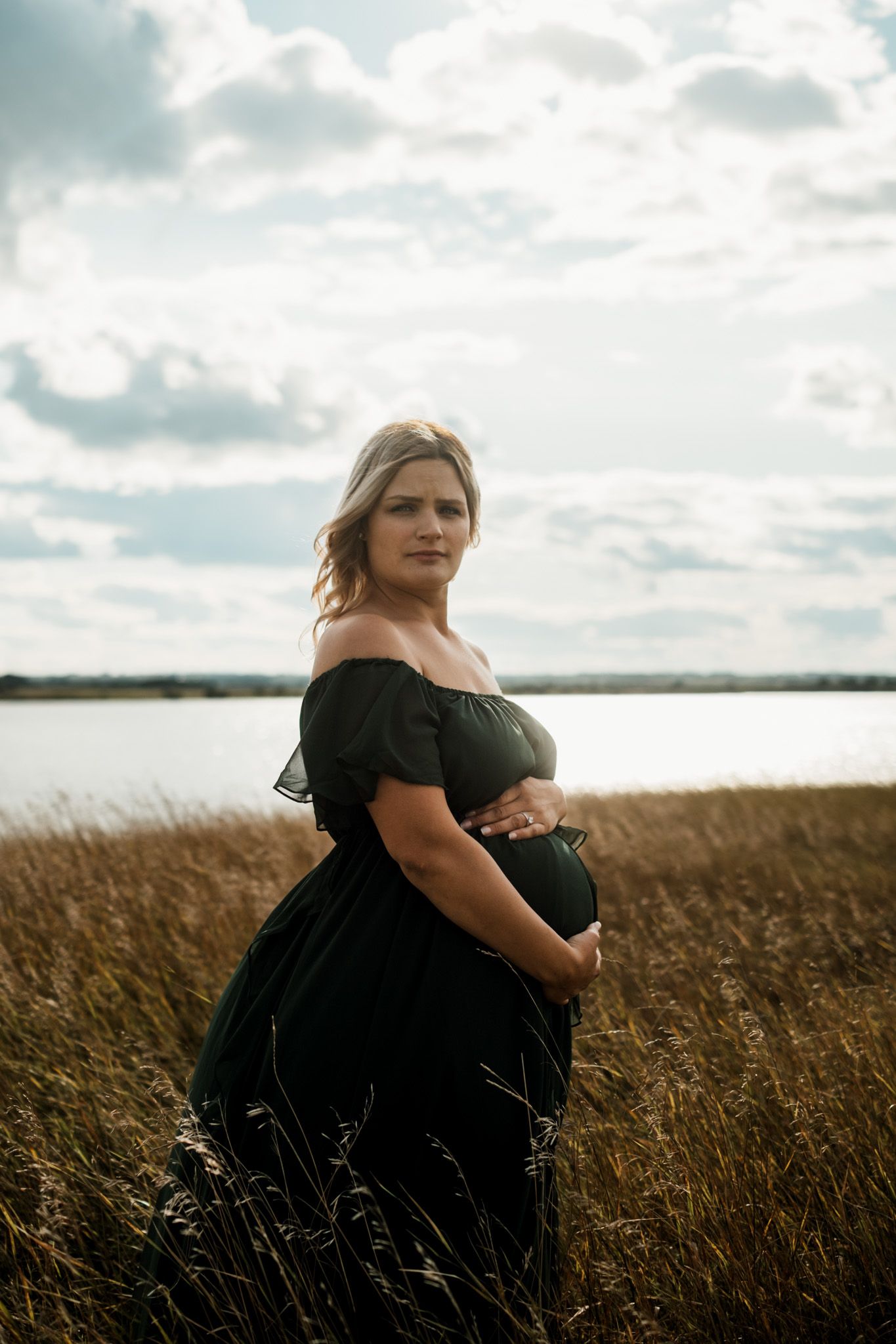 Woman in black dress poses gracefully in golden wheat field at sunset.