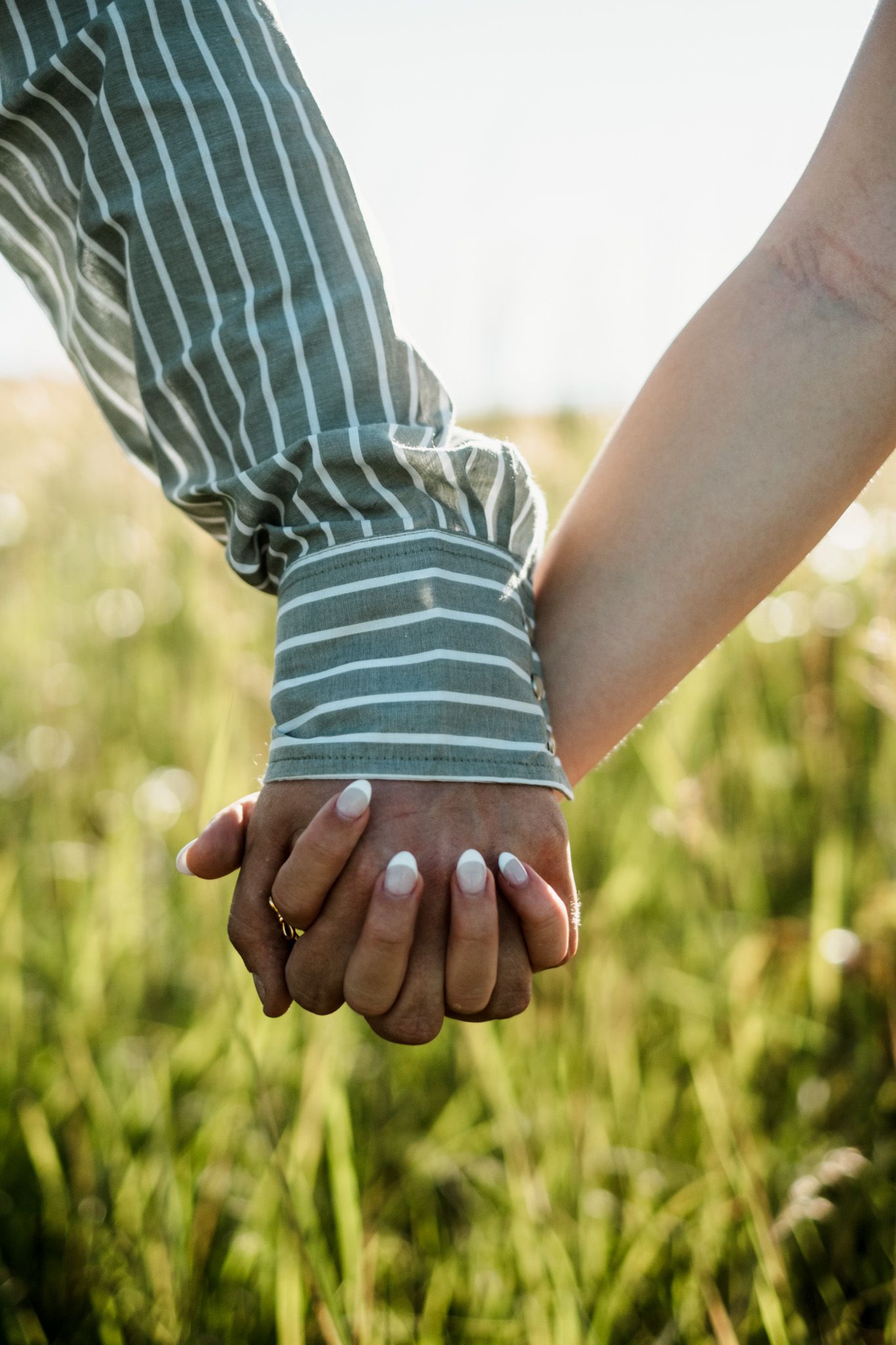 Close-up sequence of hands holding together in sunlit grass.