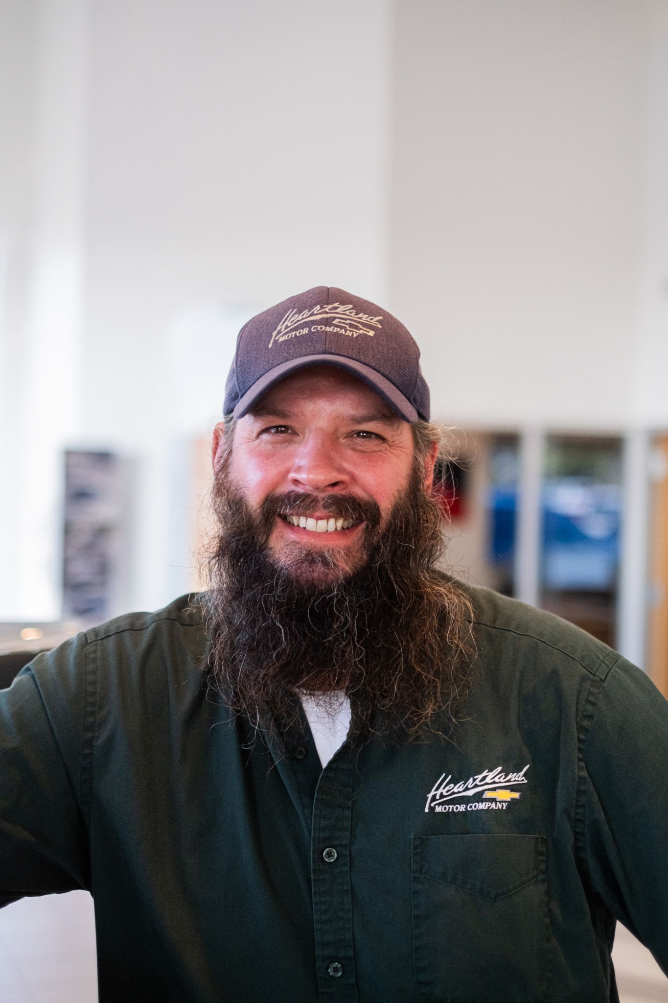 Staff member in black uniform with full beard and cap smiling at camera.