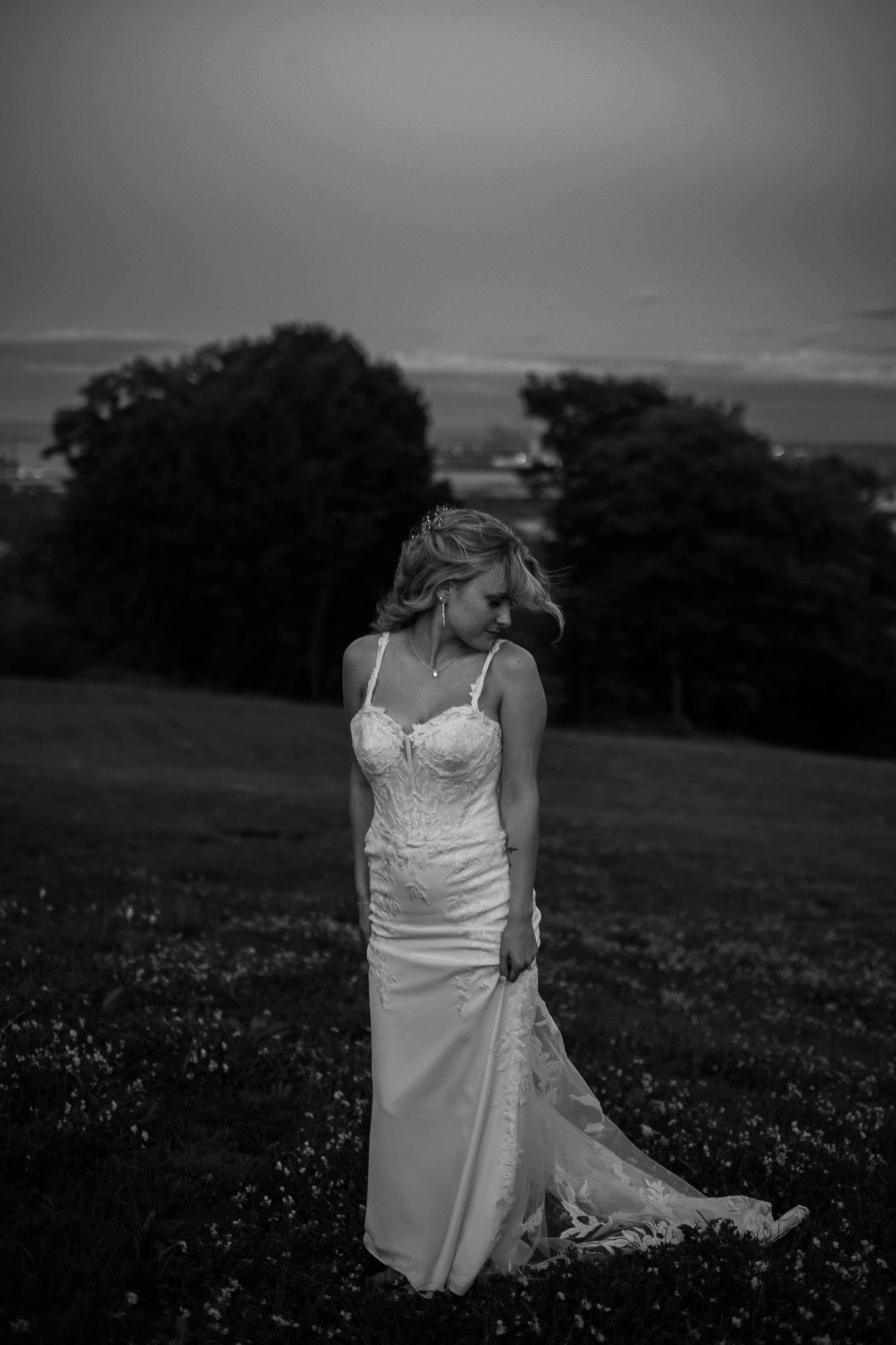 A bride in a white dress walks through a field in a series of artistic black and white photos.