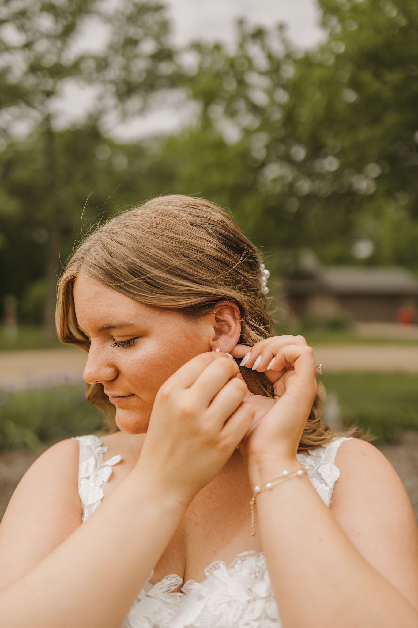 Beautiful bride in lace wedding gown putting on earrings outdoors before her wedding ceremony.