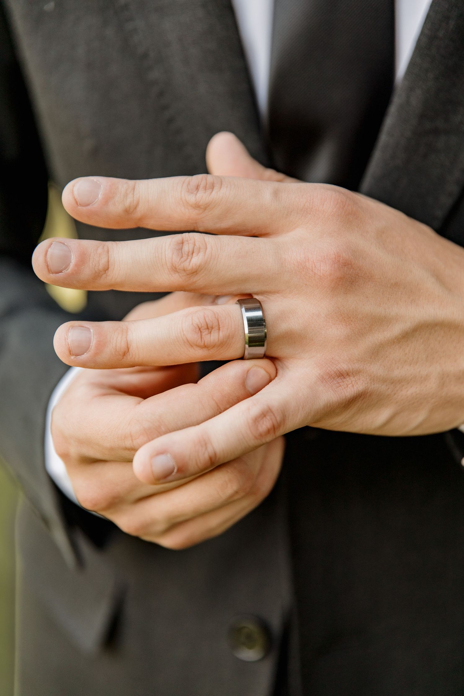 Groom in dark suit placing silver wedding band on ring finger during wedding ceremony.
