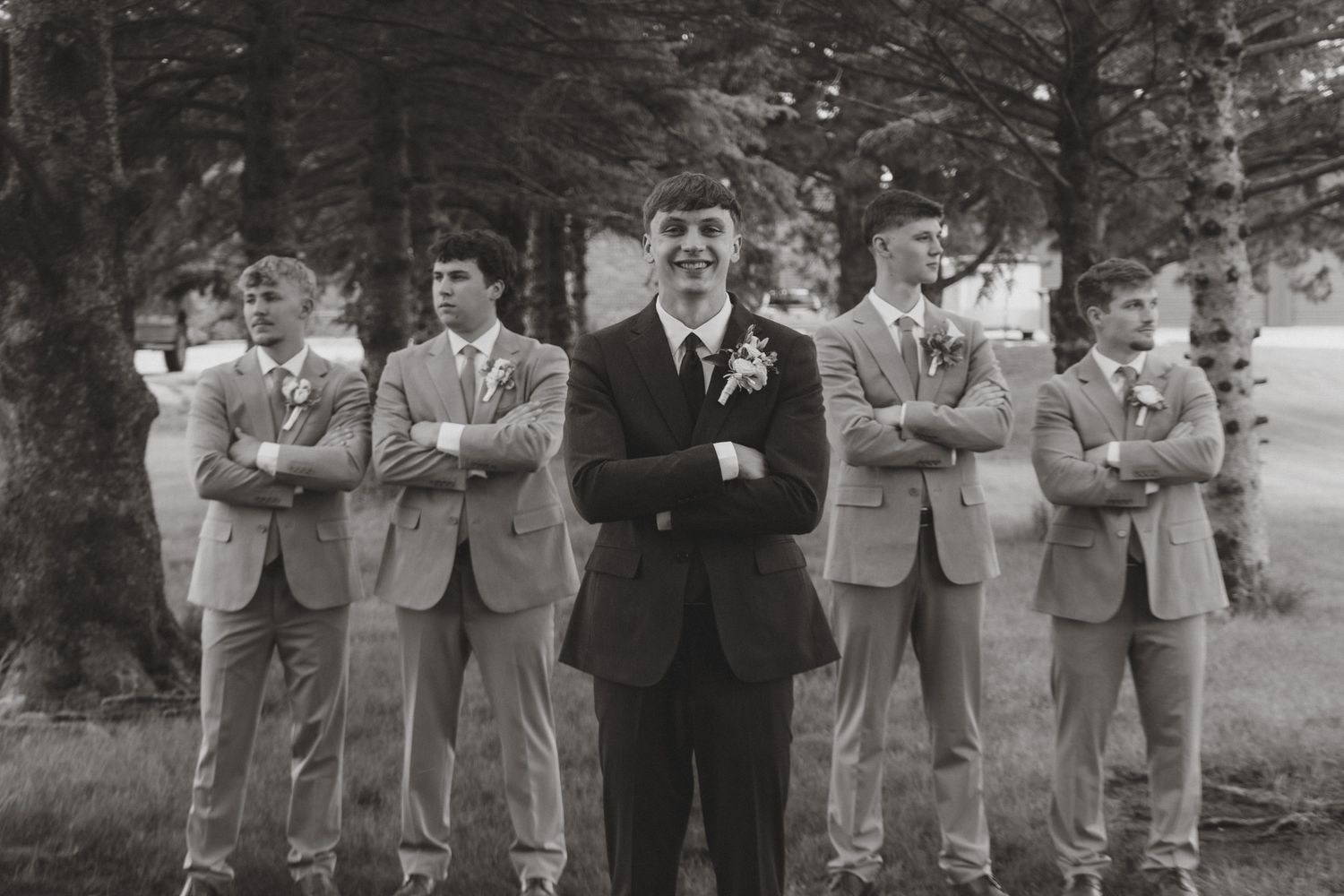 Black and white photo of a groom smiling with groomsmen in suits standing behind him outdoors.