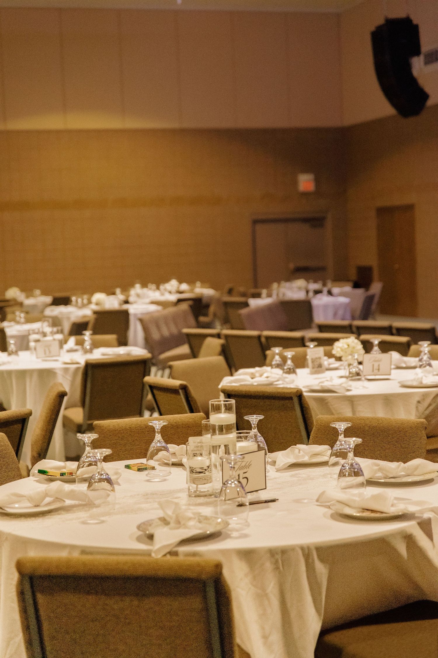 Elegant wedding reception hall with round tables set with white linens, candles, and glassware.