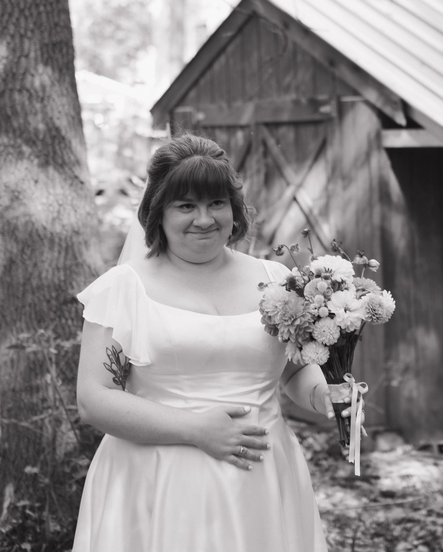 A bride in white dress holds a colorful bouquet against a rustic barn backdrop.