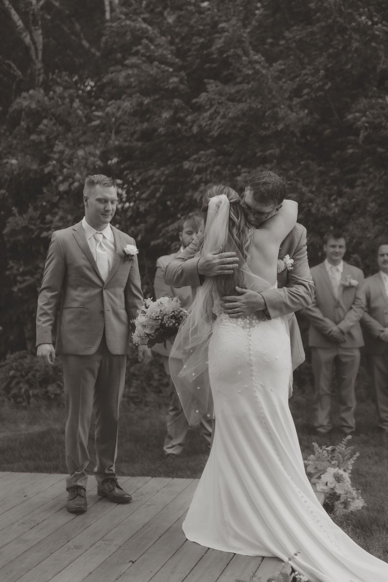 Black and white photo of bride and groom sharing first kiss at outdoor woodland wedding ceremony.