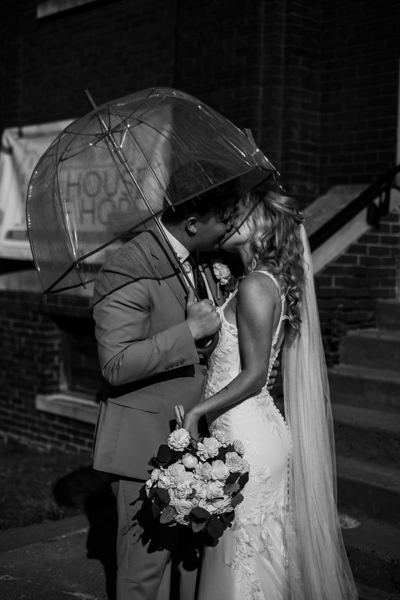 Couple sharing a romantic moment under black umbrellas in the rain.