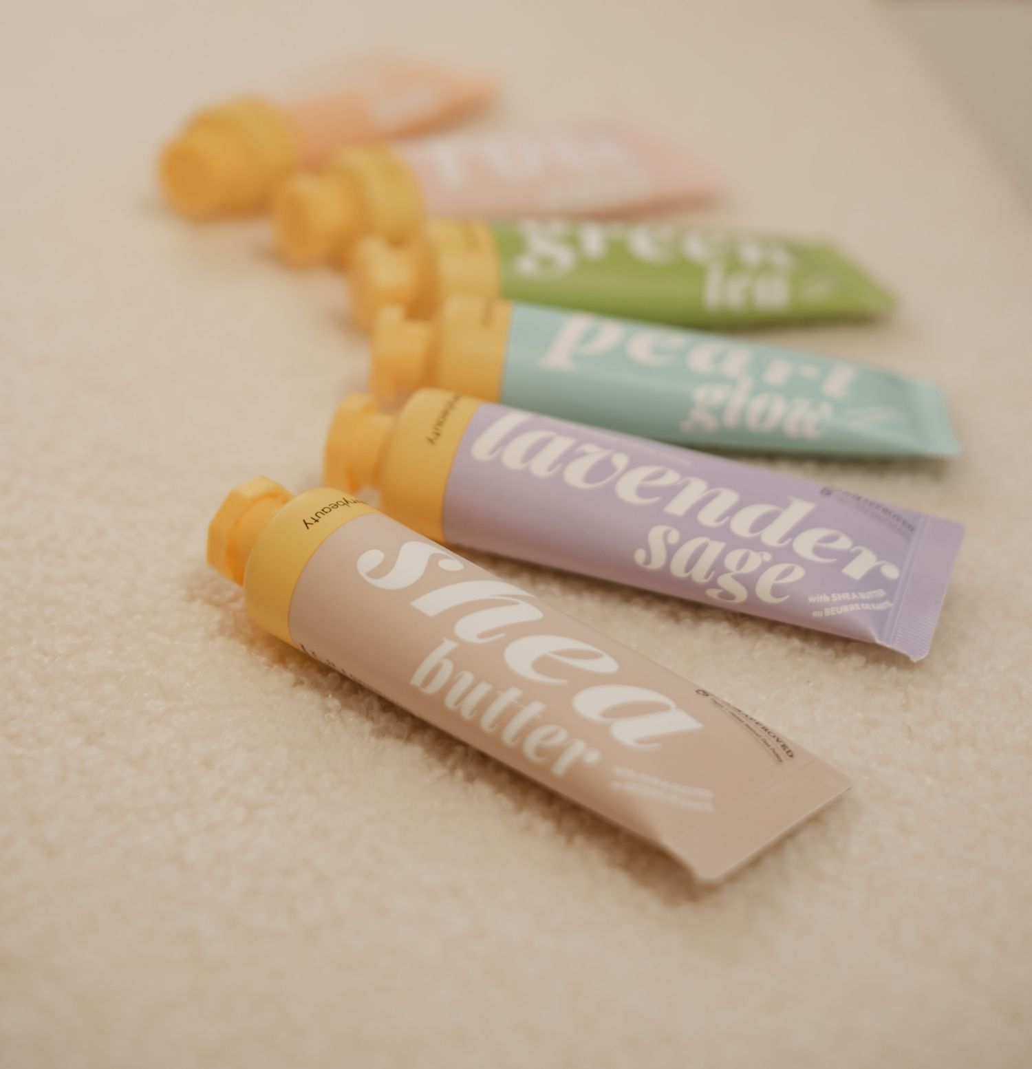 Collection of pastel colored lip balm tubes arranged on a beige surface.