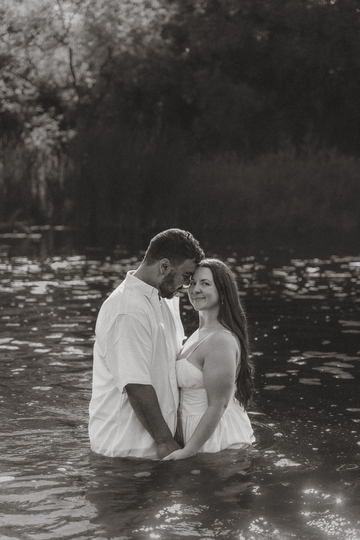 Couple in white standing in a river, sharing an intimate moment surrounded by nature.