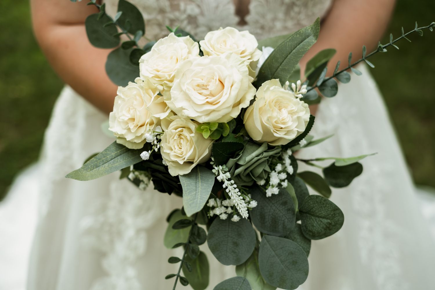 White roses and eucalyptus leaves form an elegant bridal bouquet against a white wedding dress.