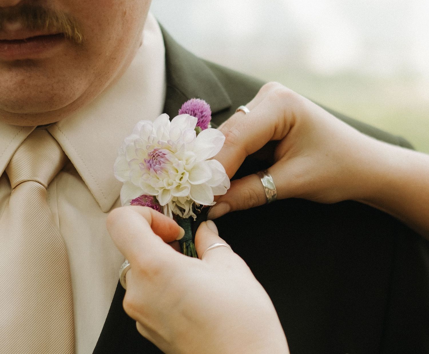 Close-up of hands pinning delicate flower boutonniere on formal attire.