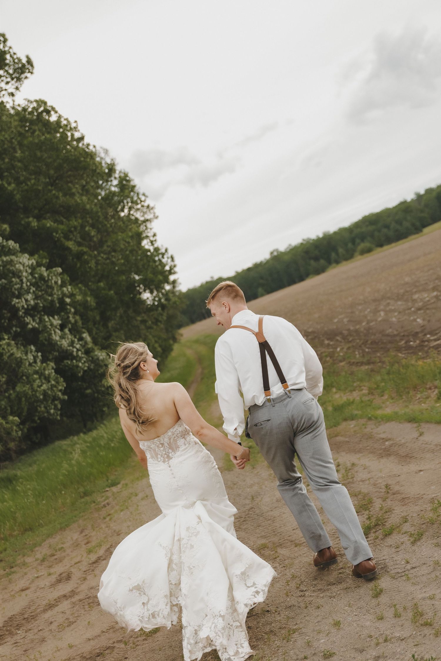 Bride and groom holding hands walking along sandy path on wedding day.