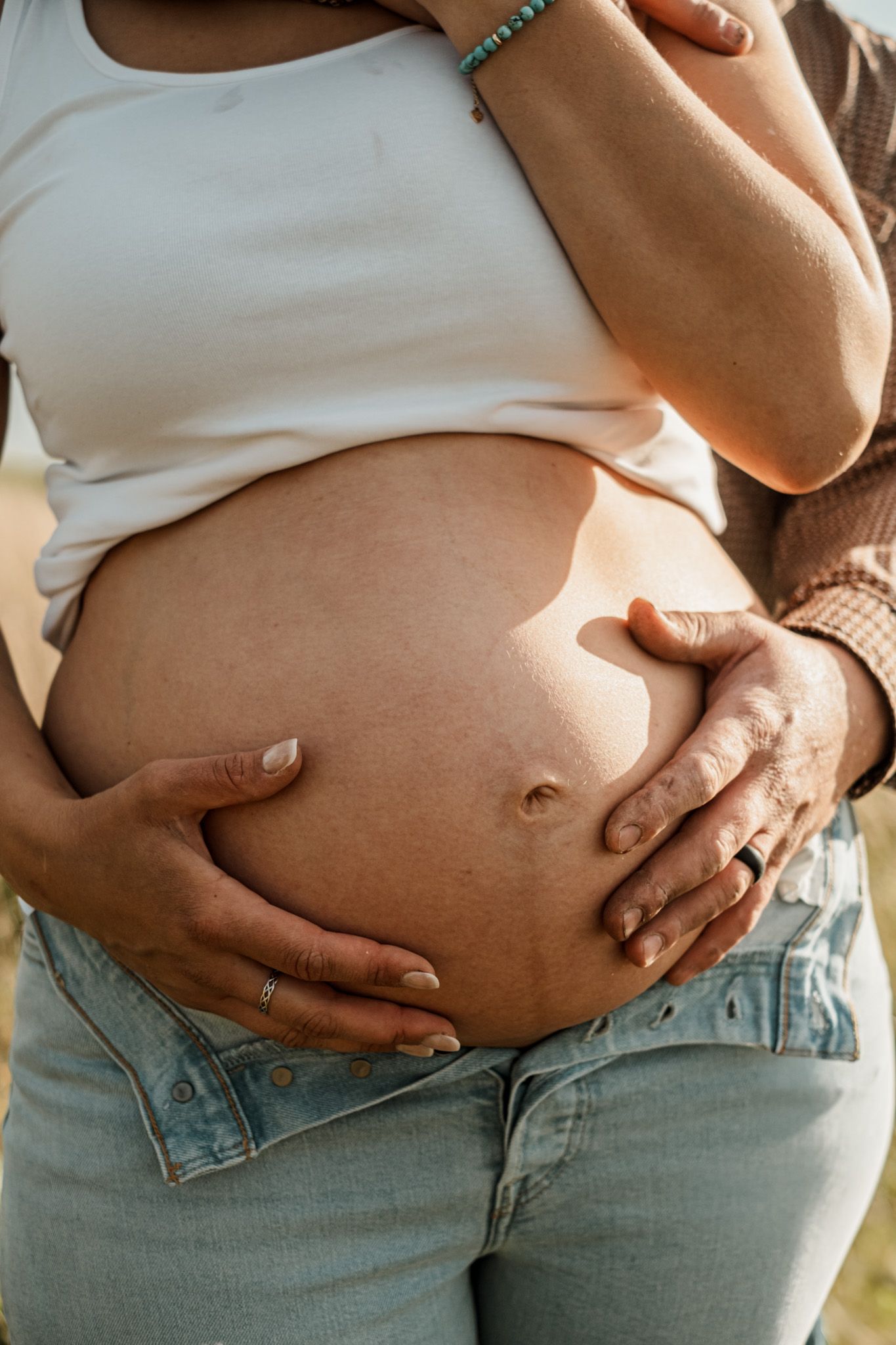Close-up shots of a pregnant belly in denim jeans against natural lighting.