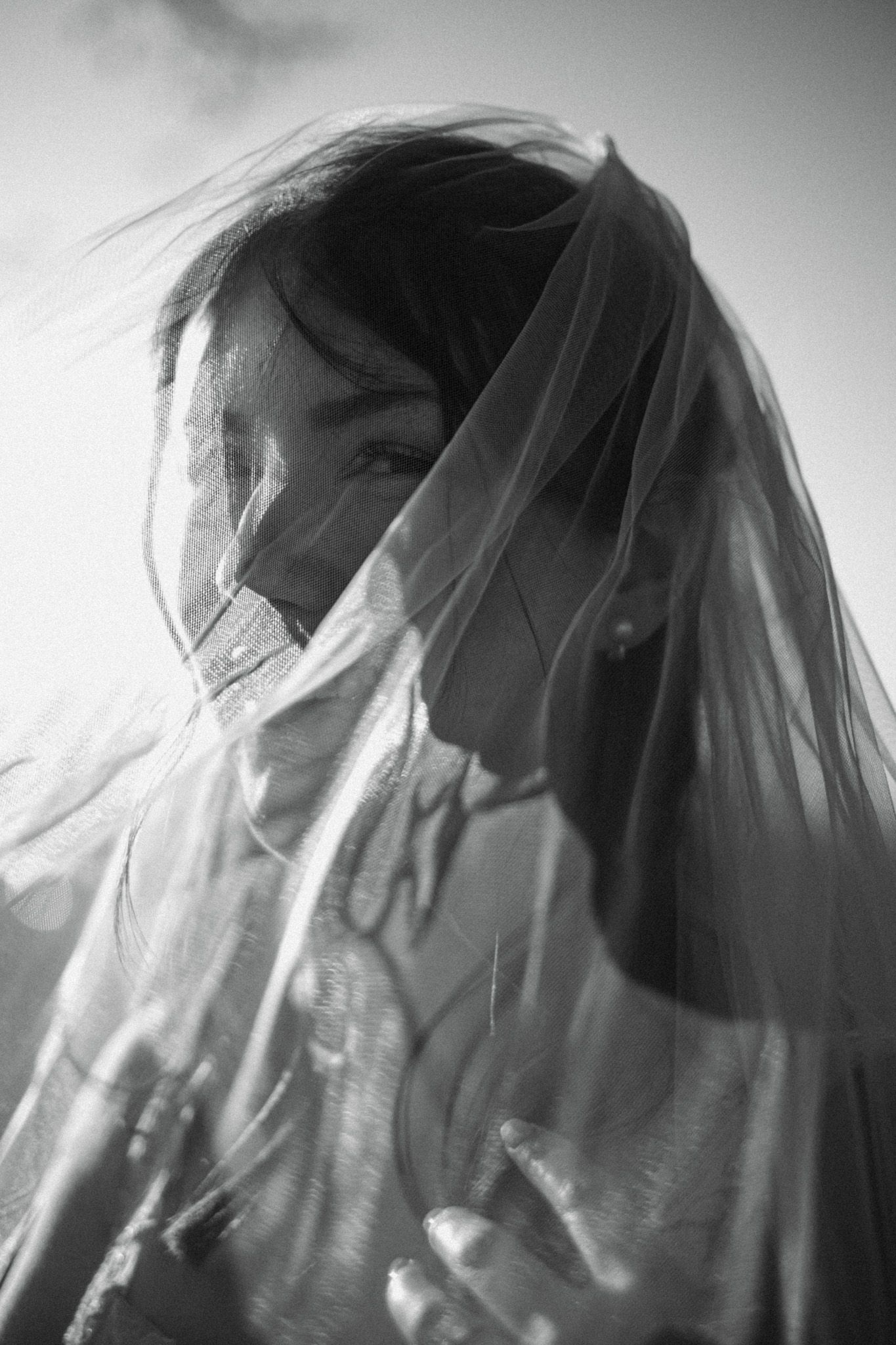 Artistic black and white close-up of bride behind flowing veil.