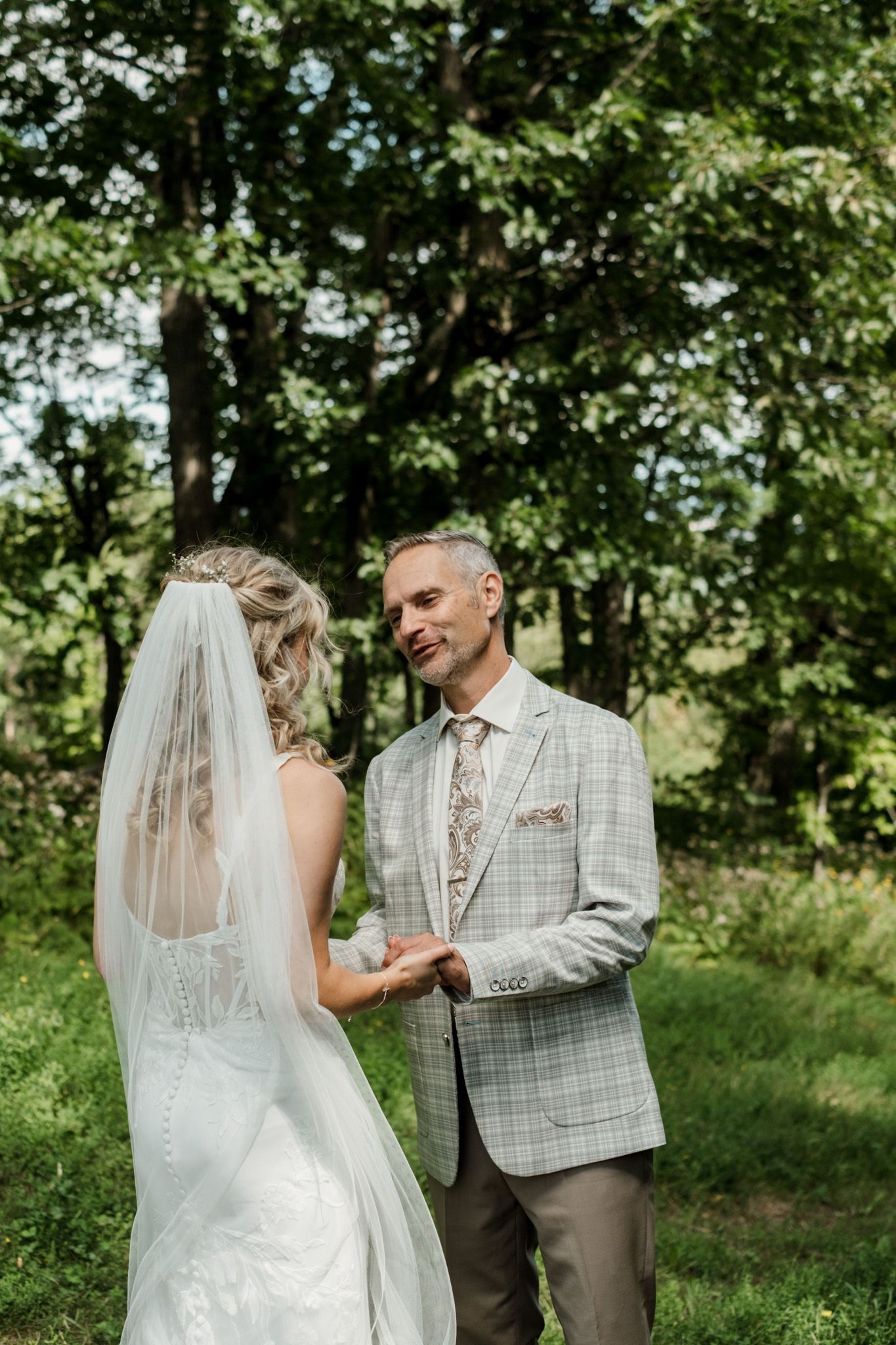 Bride in white dress shares tender moment with father during outdoor wedding ceremony.