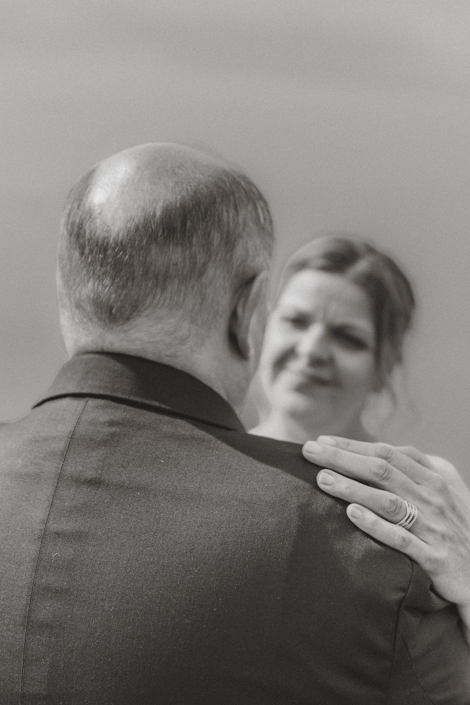Black and white wedding photo of bride placing hand on groom's shoulder, wearing stacked rings, sharing an intimate dance moment.