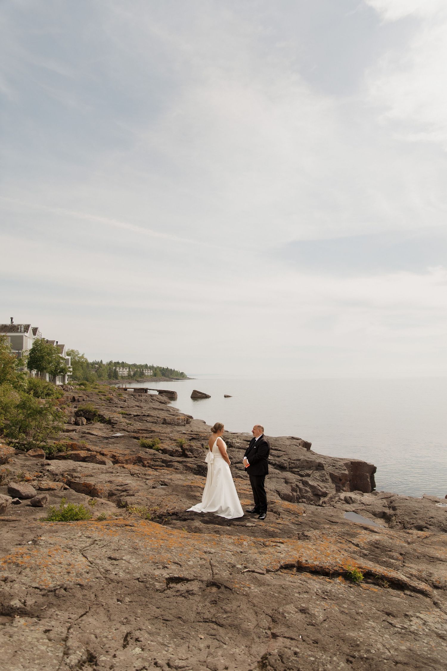 Bride and groom exchange vows on rocky shoreline with calm ocean backdrop on their wedding day.