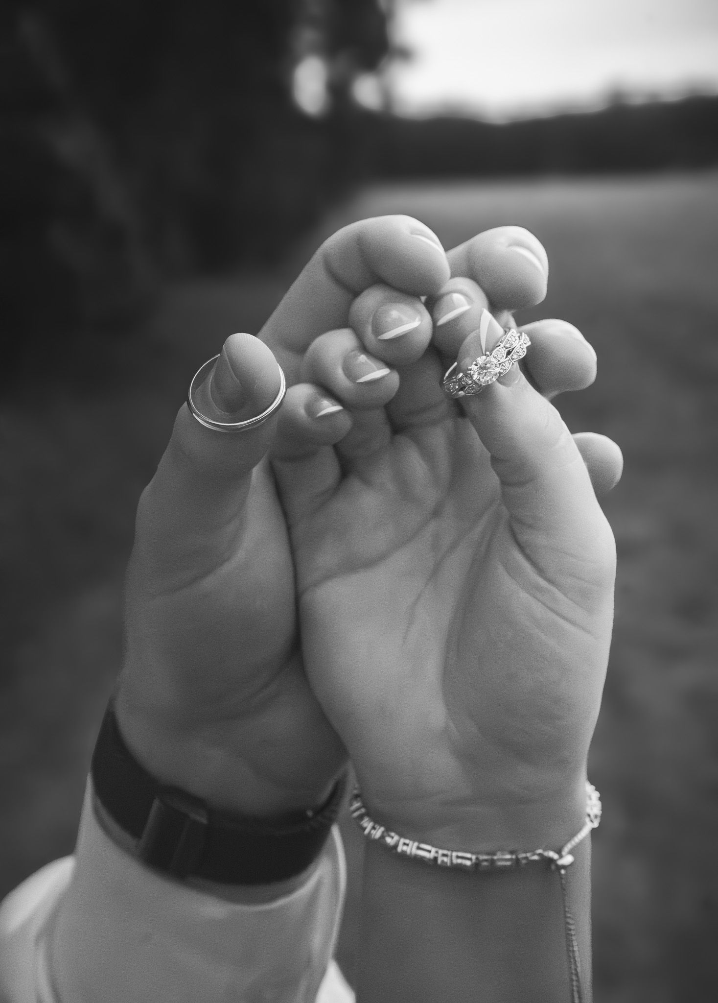 Black and white close-up of bride and groom holding hands, displaying sparkling wedding and engagement rings.