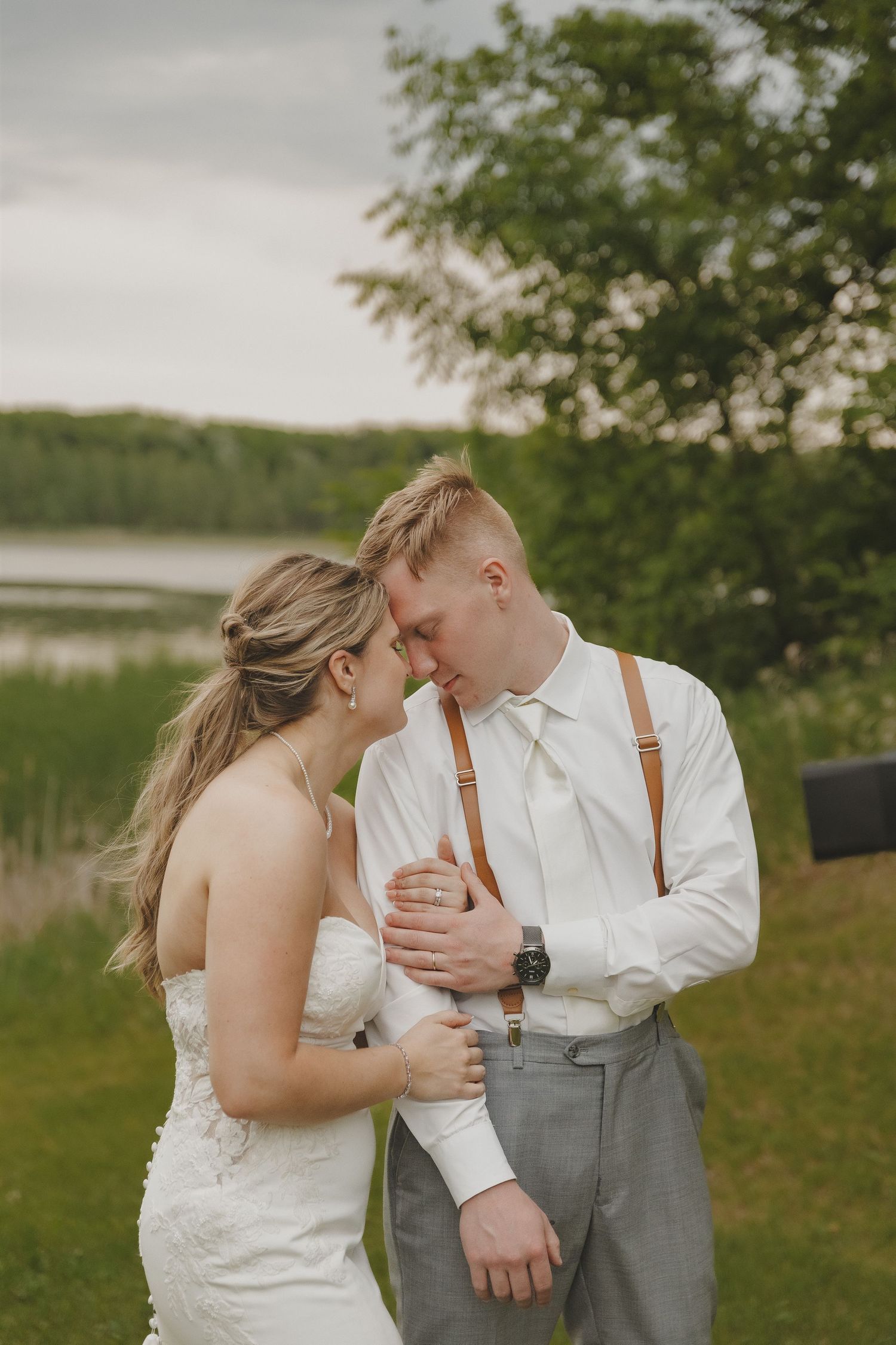 Bride and groom sharing an intimate forehead touch moment outdoors near a lake.