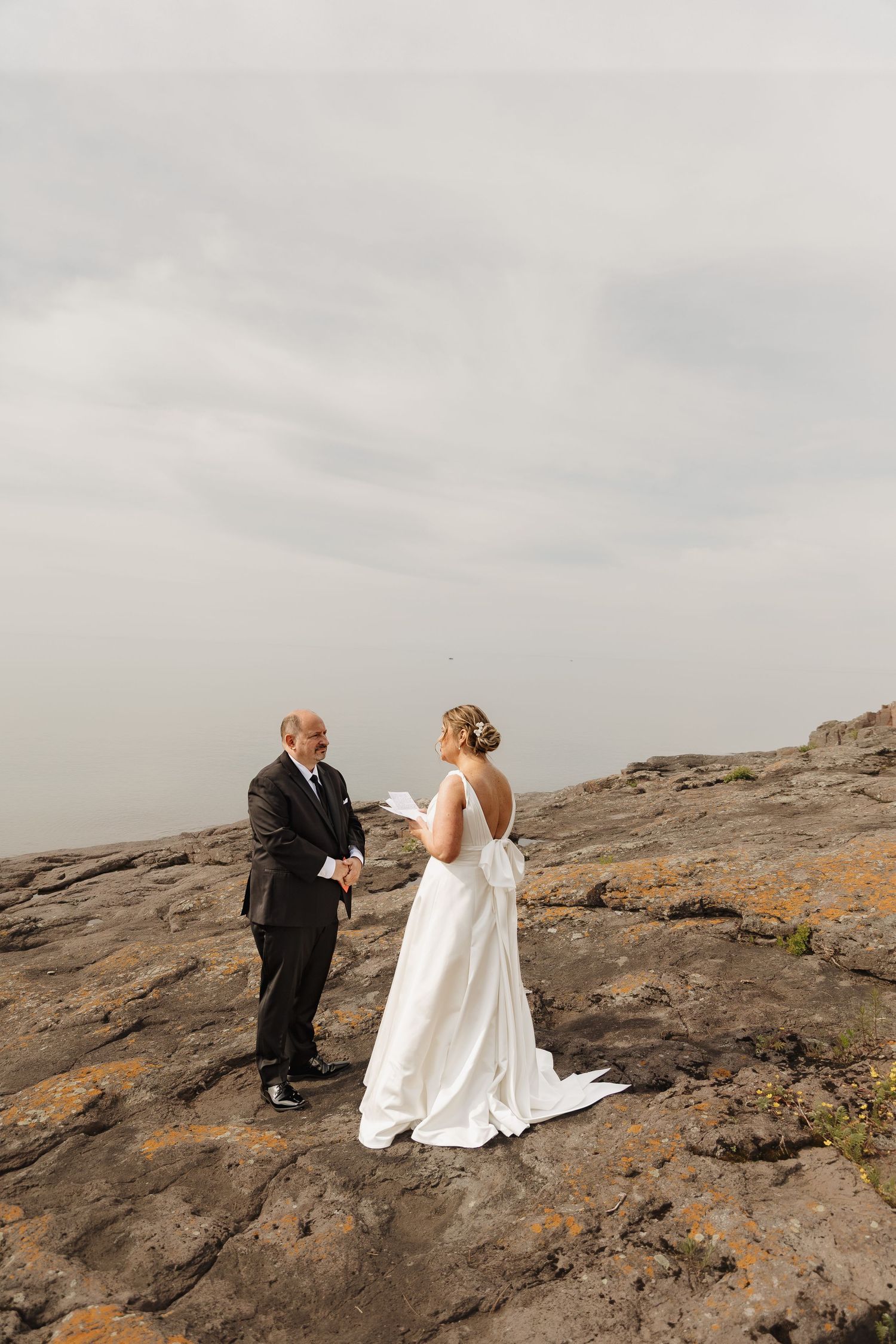 Bride and groom exchange vows on rocky cliffside under dramatic cloudy sky.