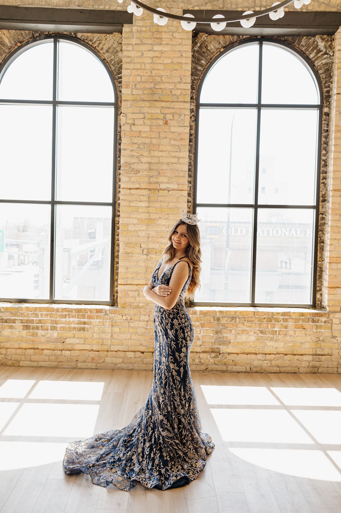 Woman in navy floral lace mermaid gown with train stands in sunlit brick loft.