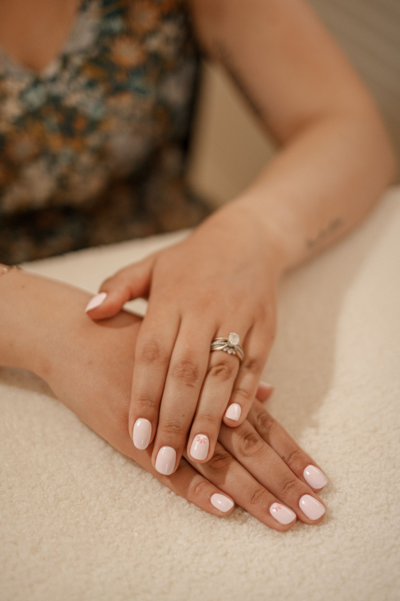 Hands with white manicure and engagement ring displayed on cream colored surface.