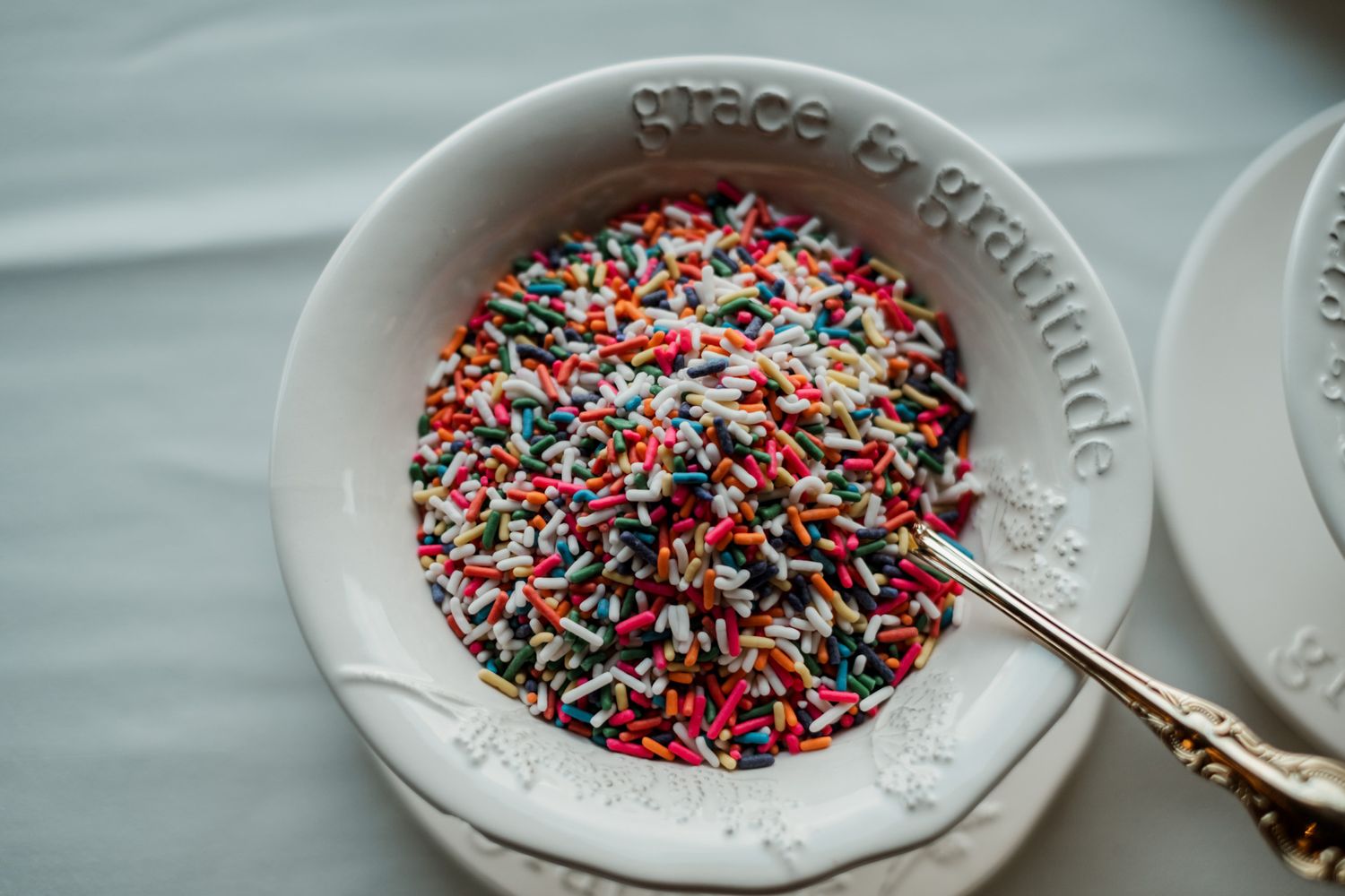 Colorful sprinkles served in white ceramic dishes at a wedding dessert table.