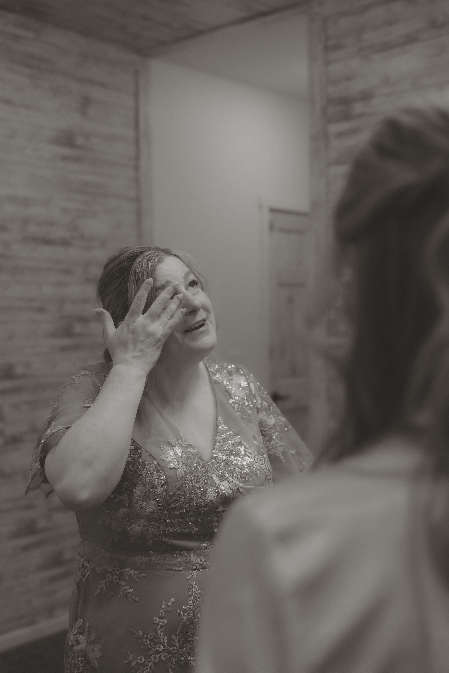 Black and white photo of an emotional woman in a sequined gown wiping tears while looking in a mirror.