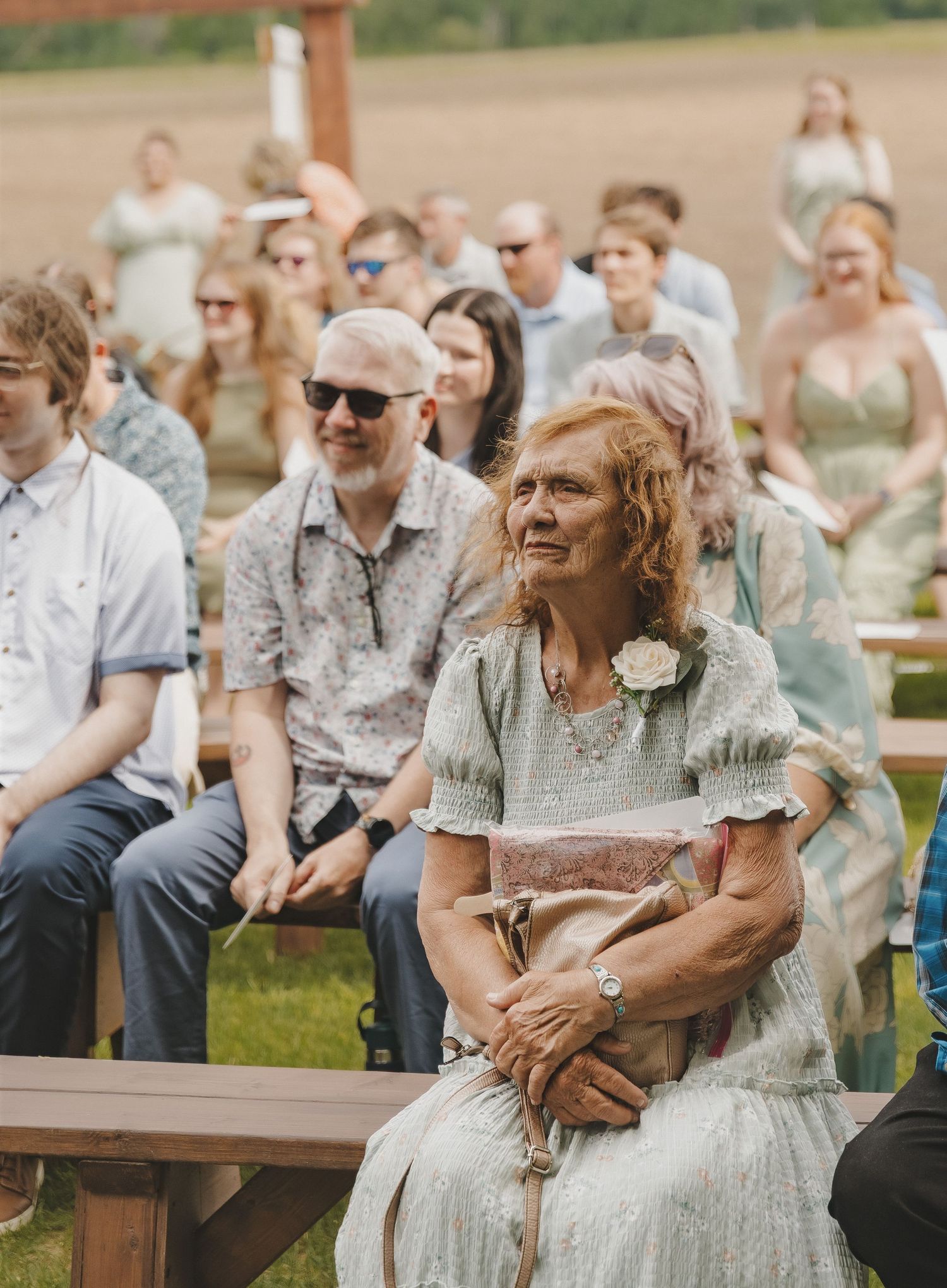 Wedding guest smiling emotionally during an outdoor ceremony with seated guests behind her.