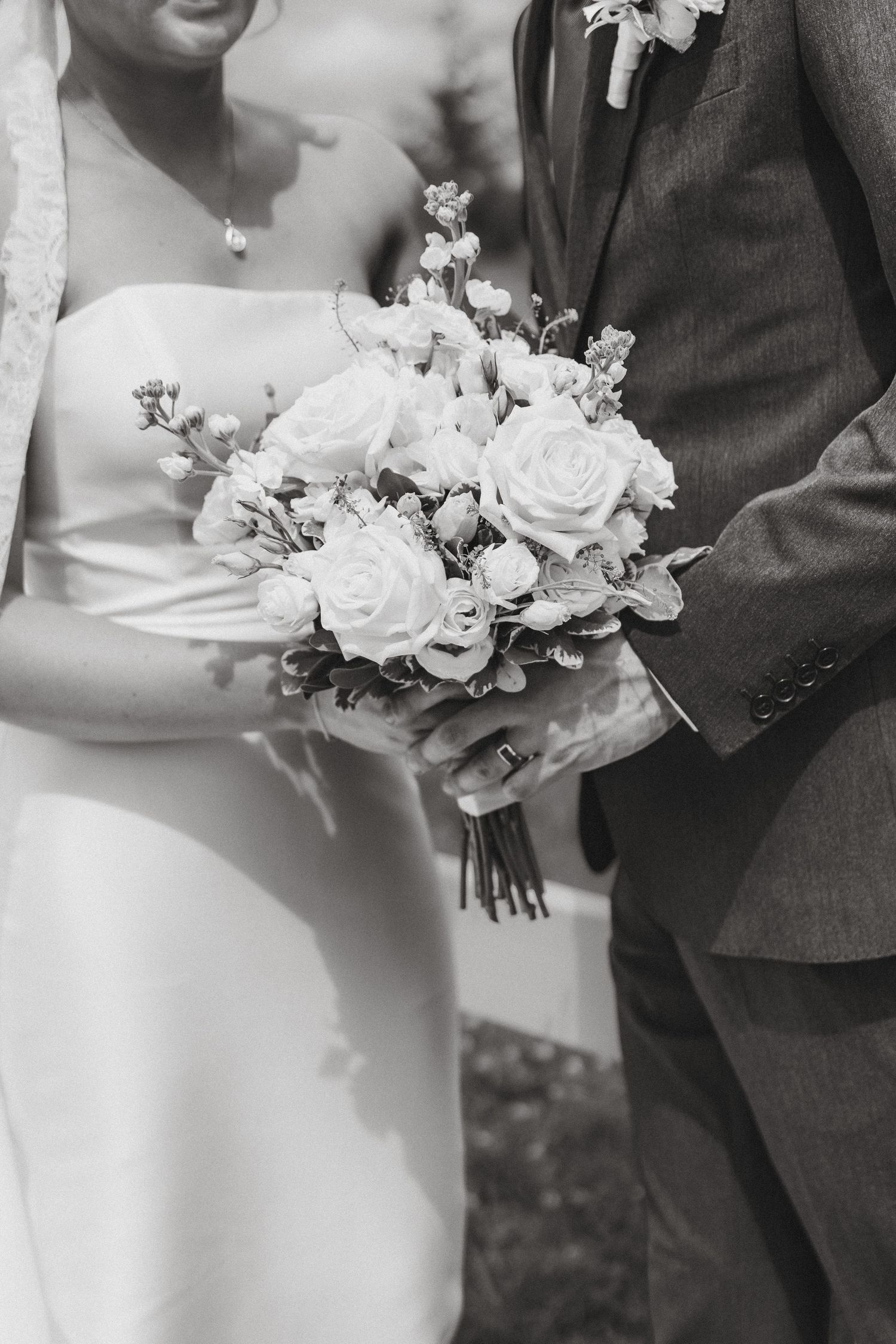 Bride and groom holding white rose wedding bouquet together in black and white photo.