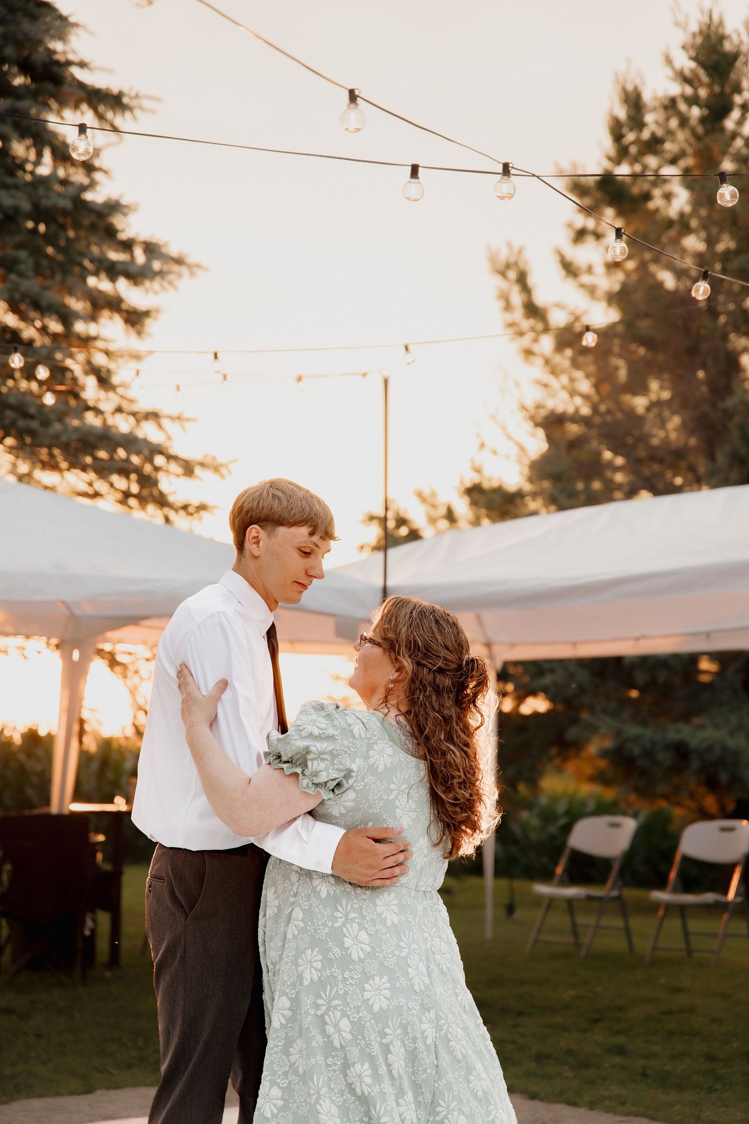 Bride and groom share a tender outdoor dance at sunset wedding reception under warm string lights.