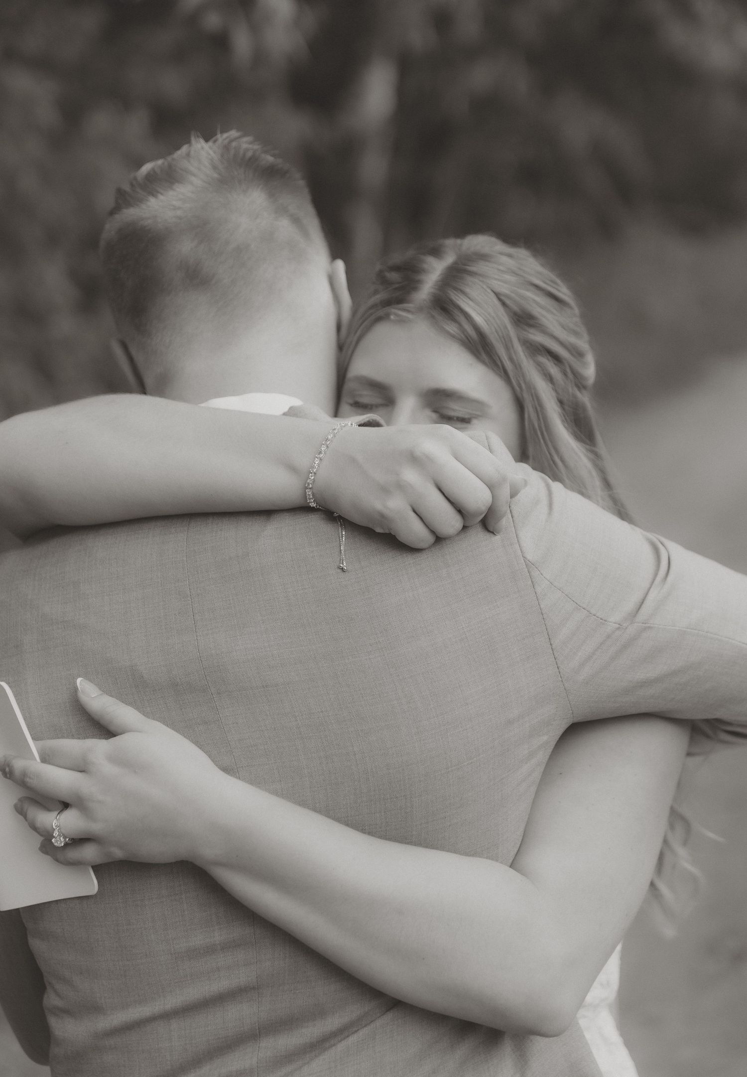 Black and white photo of bride and groom sharing an emotional embrace outdoors.