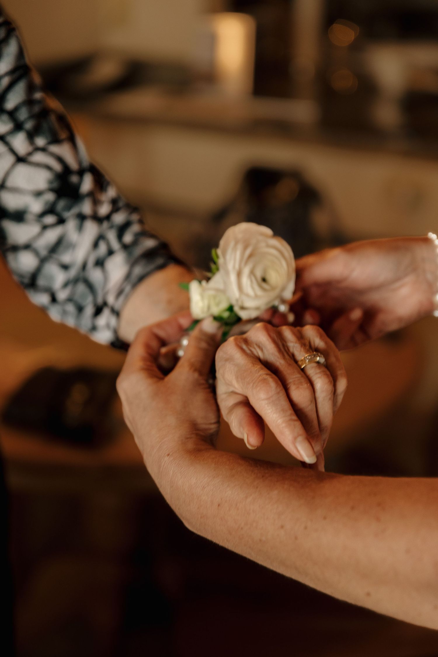 Close-up of hands attaching a white rose wrist corsage at a wedding celebration.