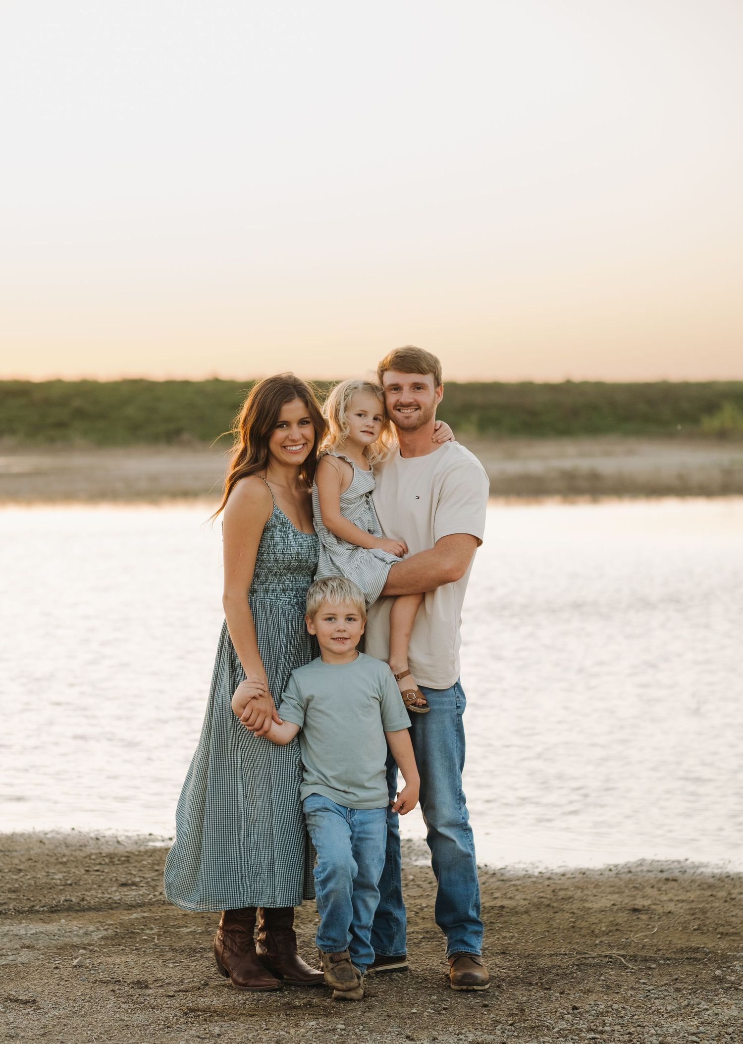 Family of four posing together by a lake during sunset.