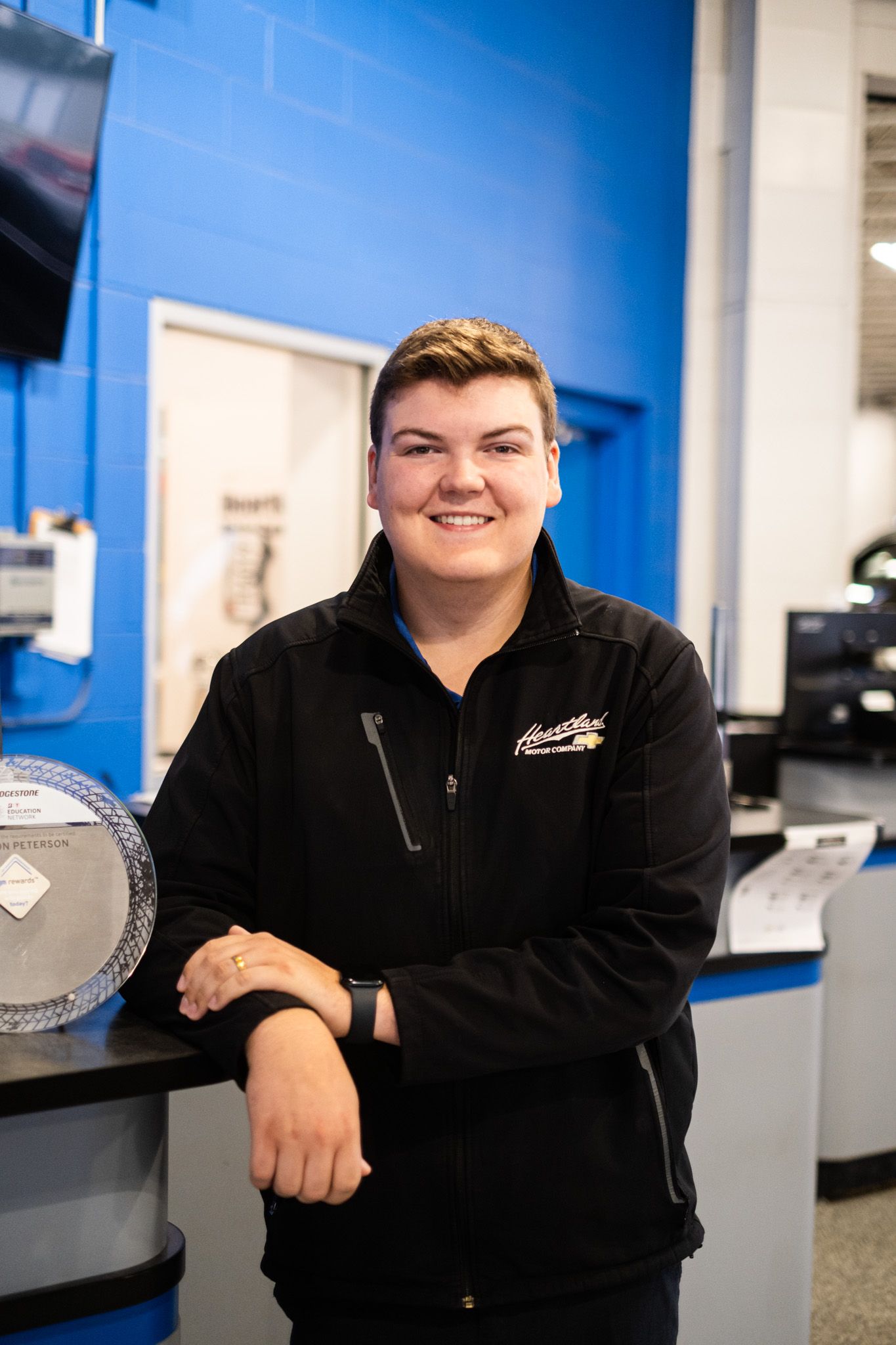 Staff member in black uniform smiling enthusiastically in dealership showroom.