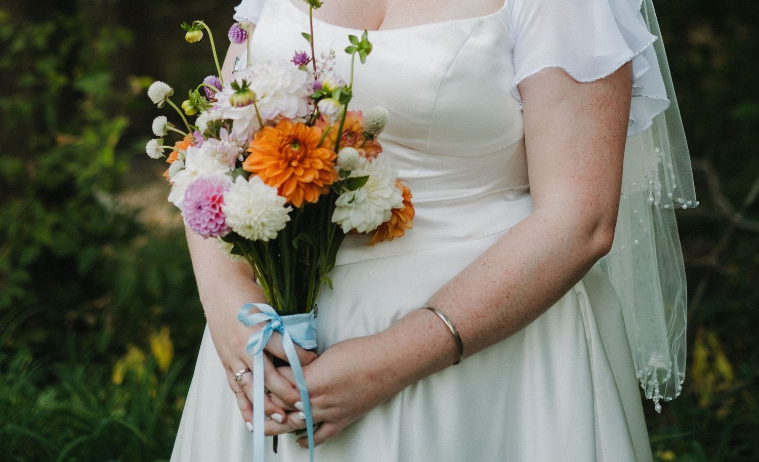 Close-up of bride holding colorful wedding bouquet with orange and white flowers.