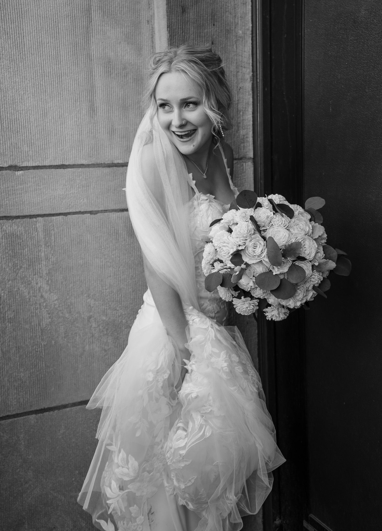 A bride in a flowing white wedding dress holds a bouquet while posing in a classic black and white portrait series.