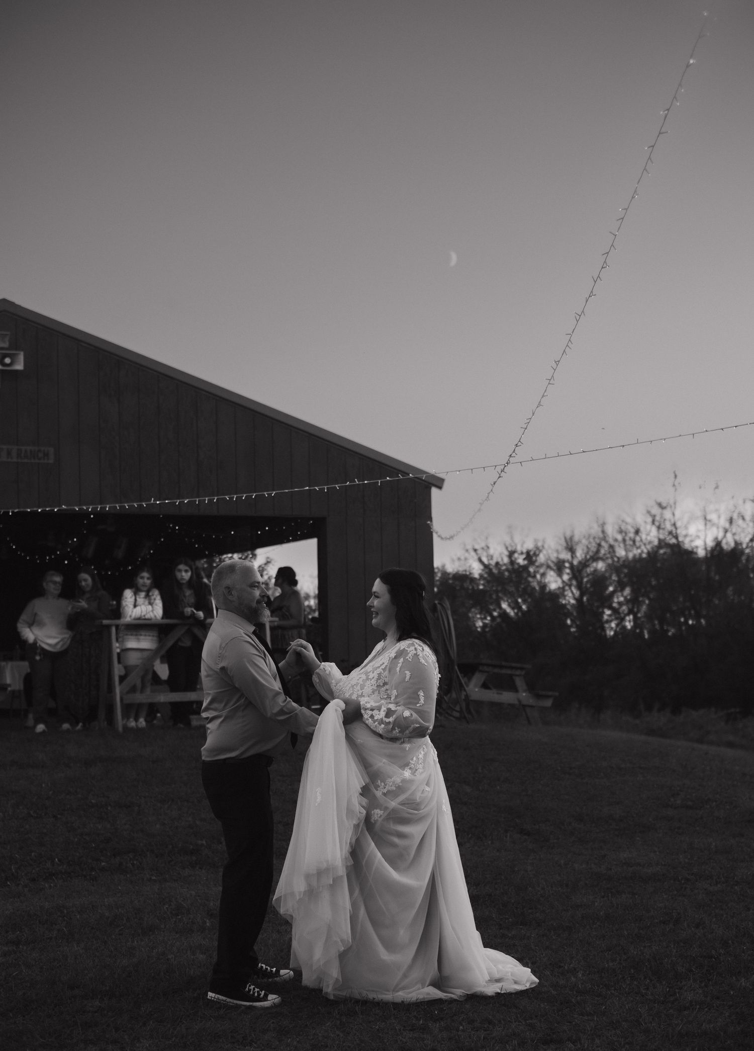 Wedding celebration at dusk with string lights illuminating a rustic barn venue.