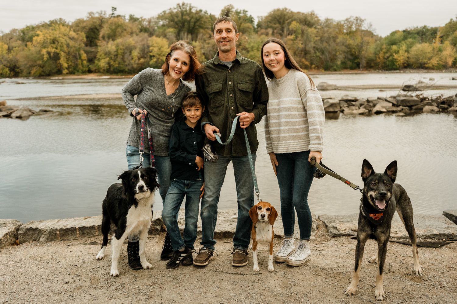 A family and their two dogs pose together on a rocky beach during autumn.