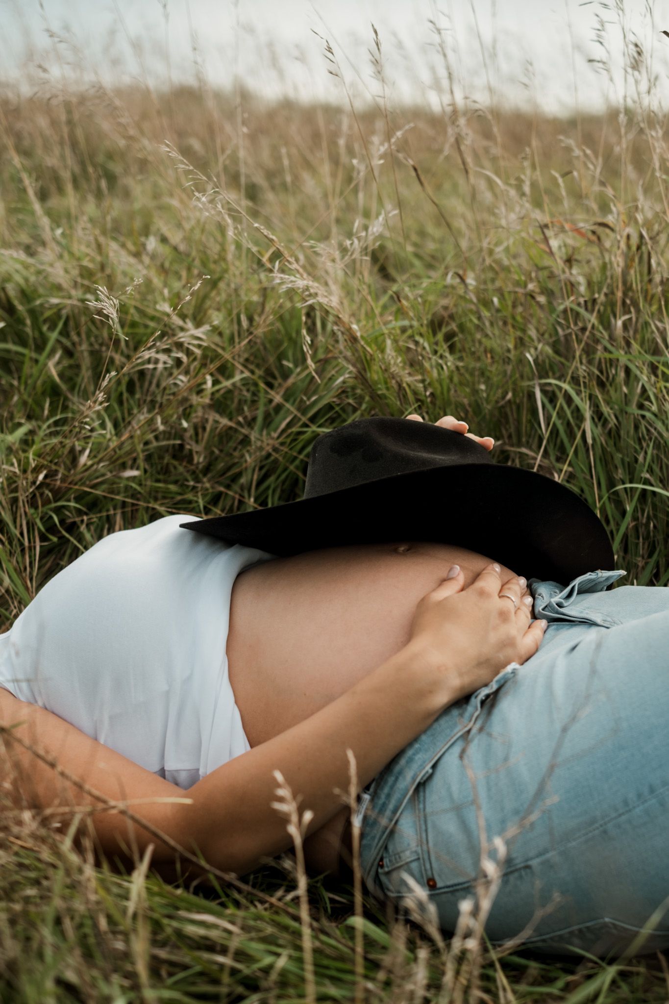 Side view of a pregnant figure lying in tall grass during golden hour.