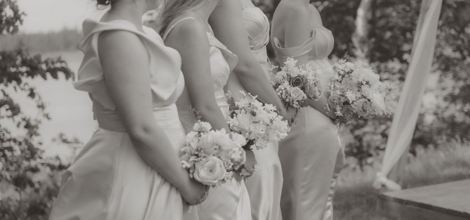 Three bridesmaids in white gowns holding floral bouquets pose together at an elegant outdoor wedding.