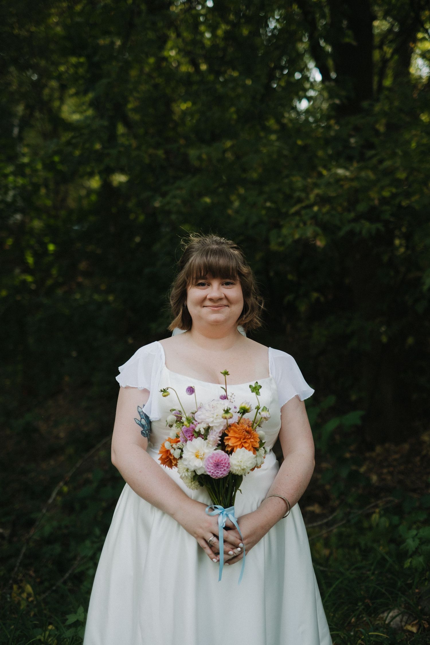 Person in white dress holds colorful summer bouquet in garden setting.
